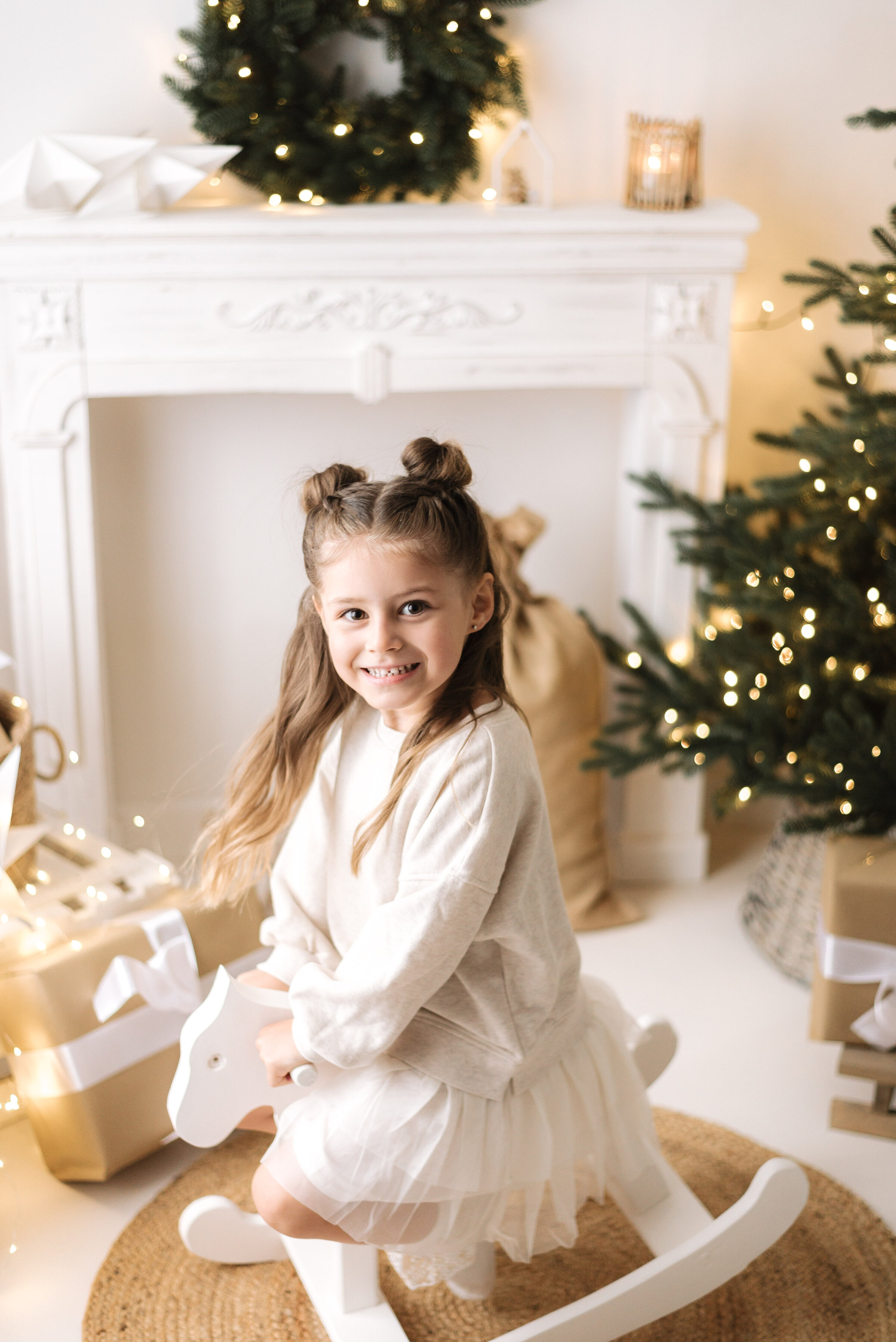 Girl on a rocking horse smiling infront of a christmas tree at a christmas family photoshoot in Billingshurst