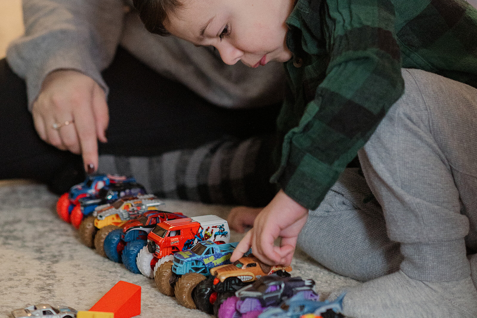 Hands of a child and parent building with colorful trucks on the floor during an at-home family photography session in Lancaster, PA.