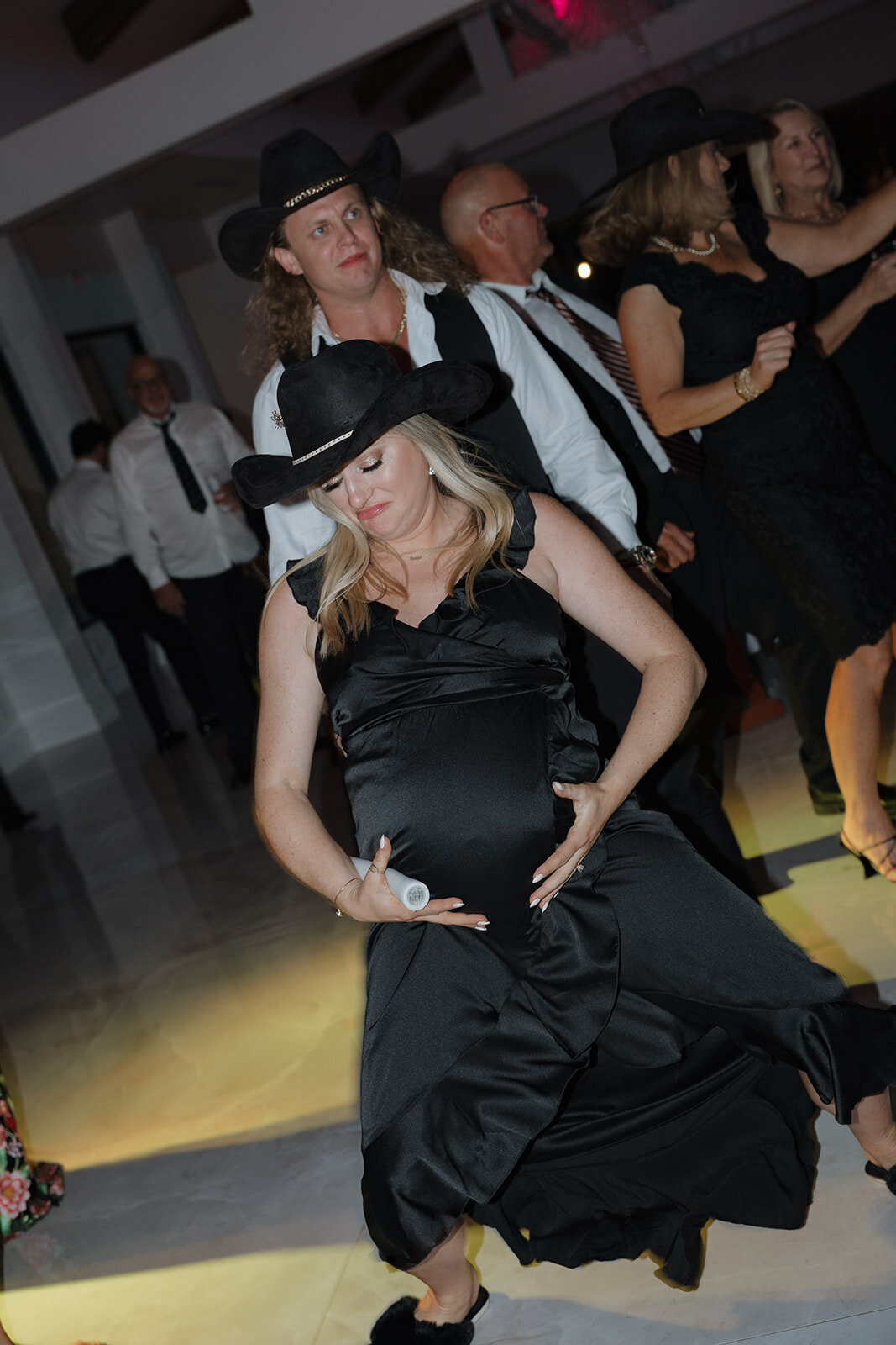 A pregnant bridesmaid rubs her belly while dancing at the reception.