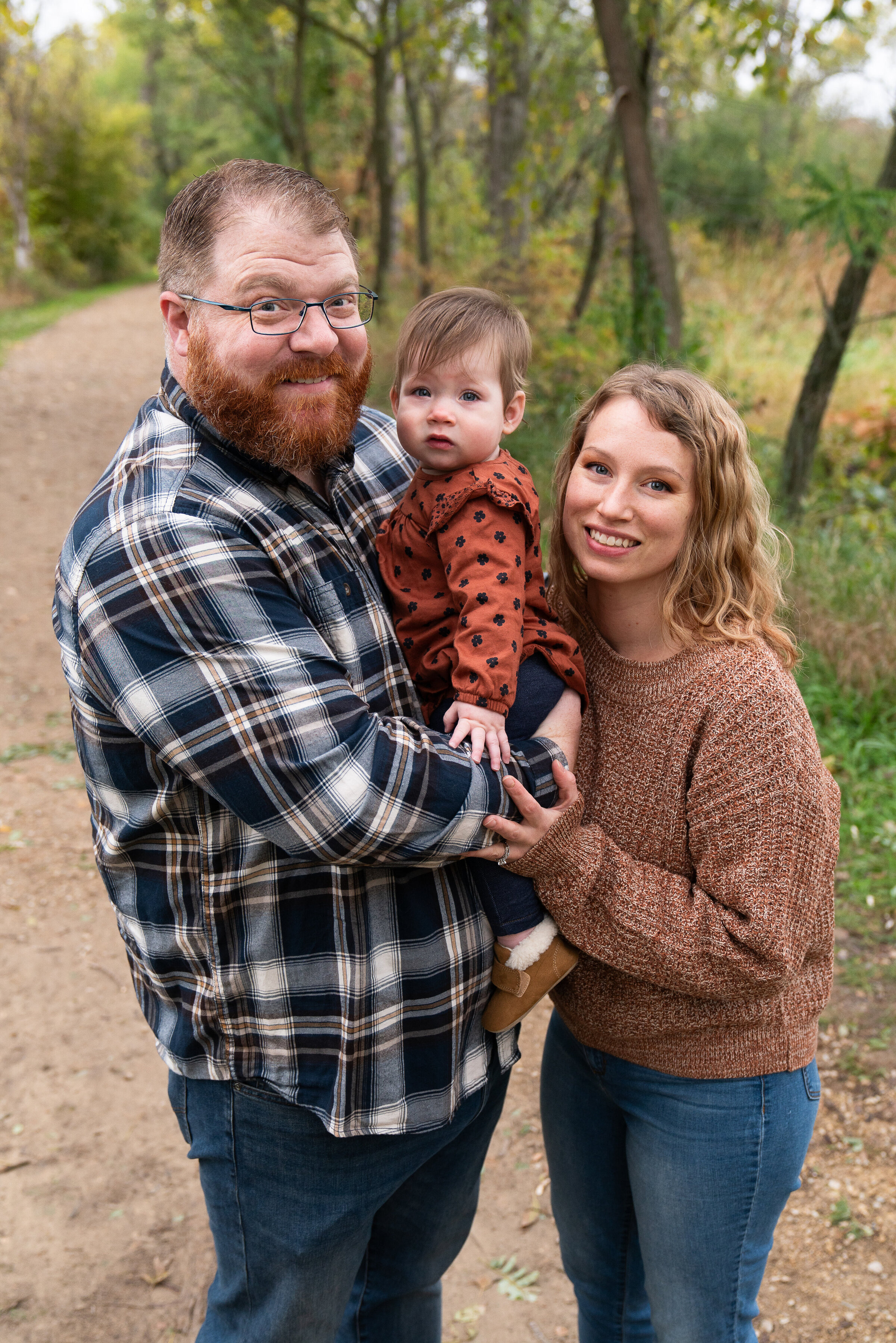 Family of three stand together and smile at the camera during their fall family photo shoot.