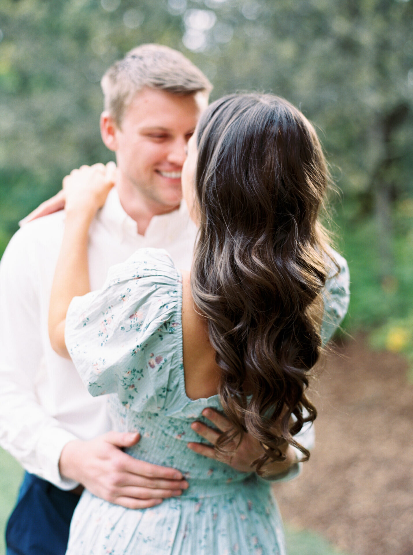 cascading hair waves down womans back as she is held by her fiance