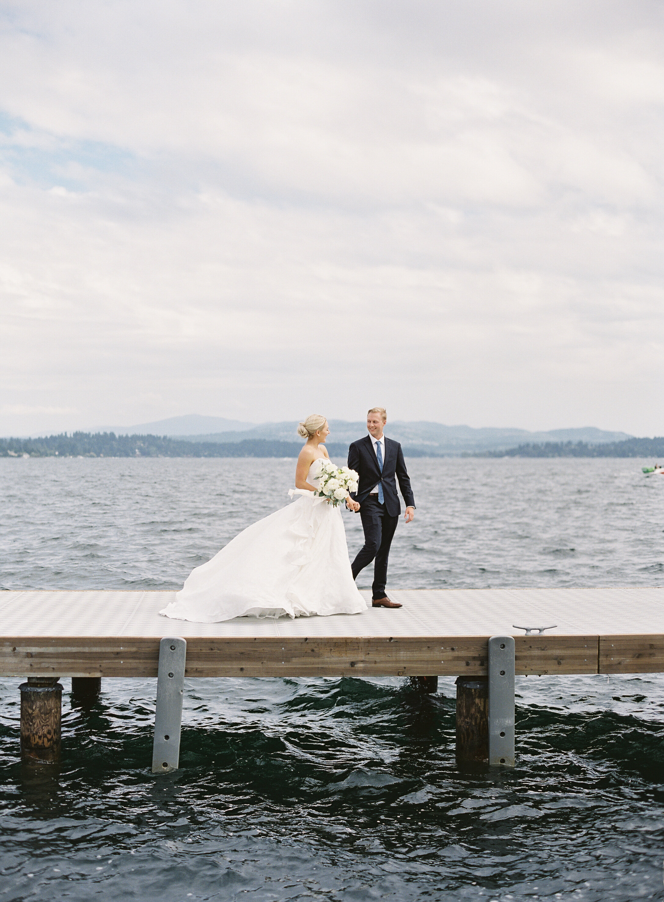 bride and groom walk hand in hand on dock on lake washington at seattle tennis club
