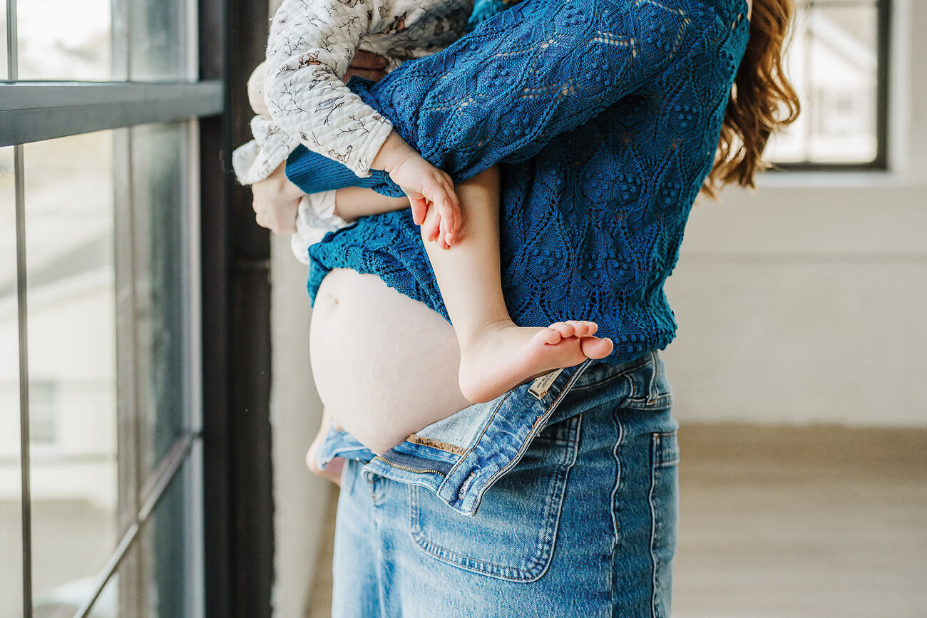 mother's bare pregnant belly with toddler feet hanging down