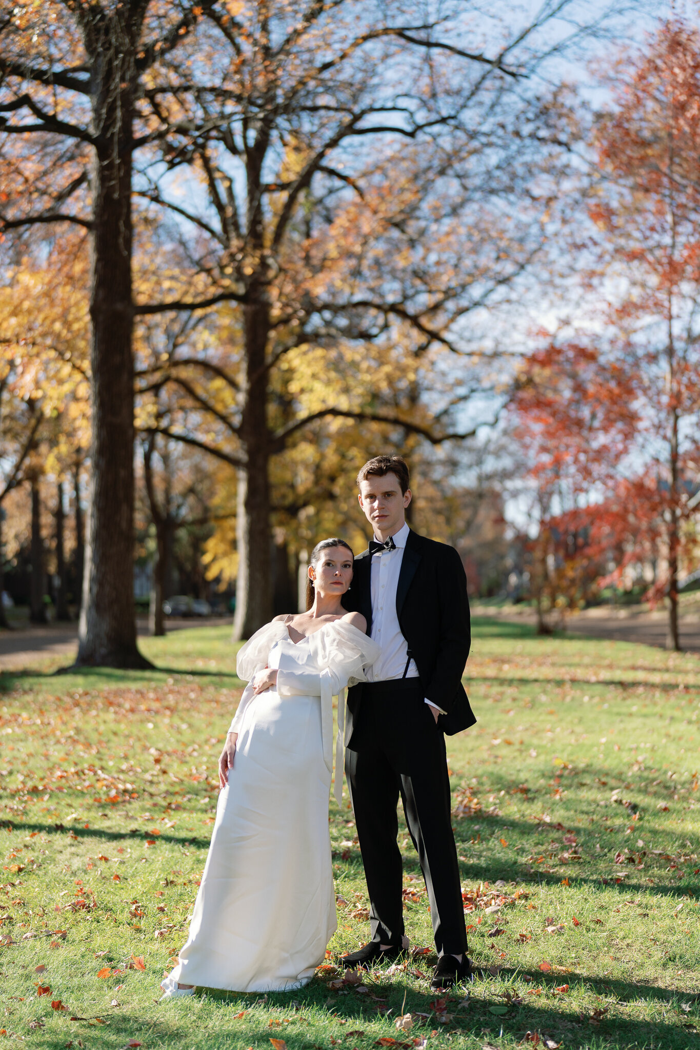 Bride and groom pose elegantly in a sunlit autumn landscape