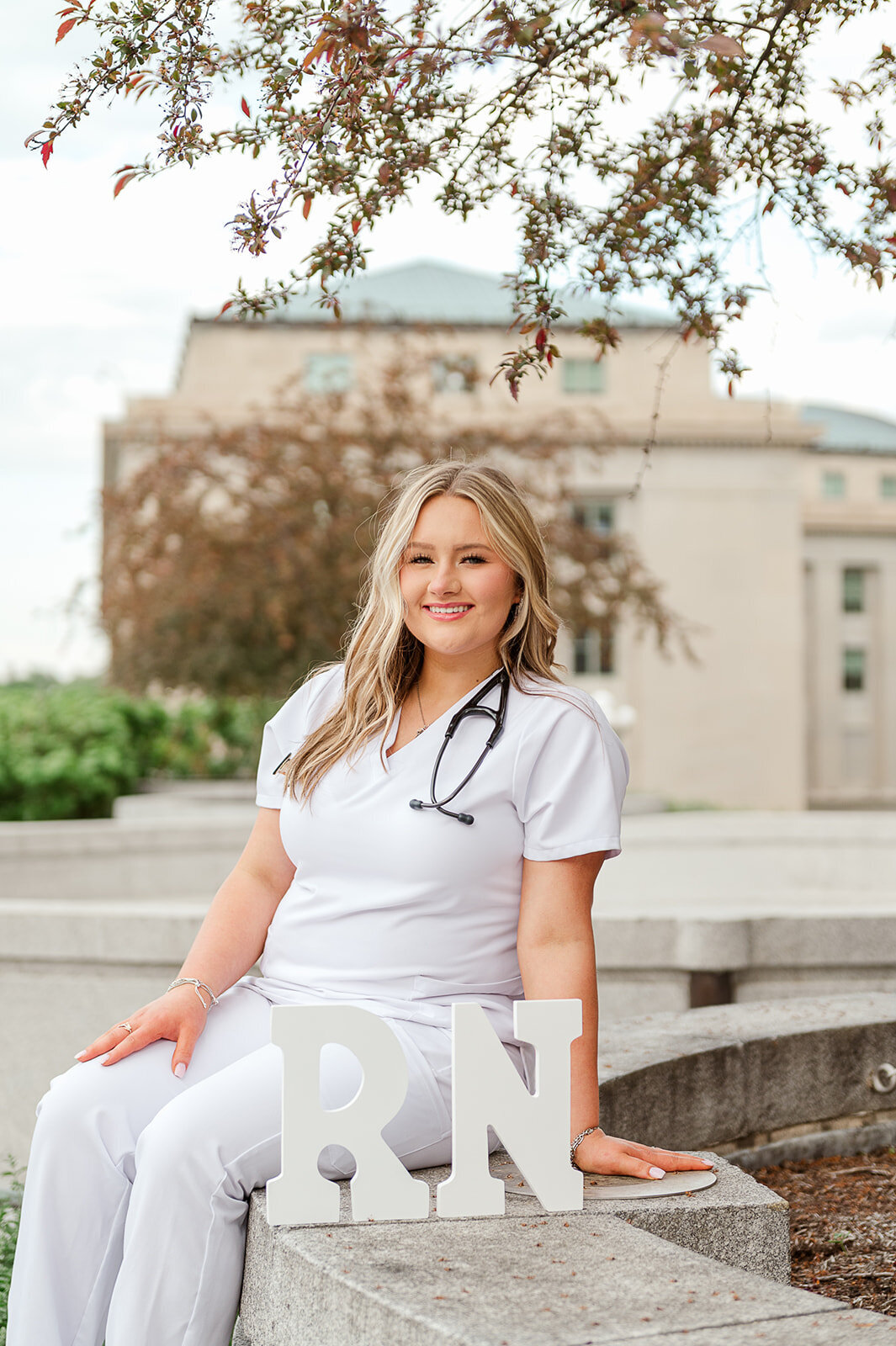 Senior girl in a white nursing dress sitting on steps near a college campus in Baltimore, MD