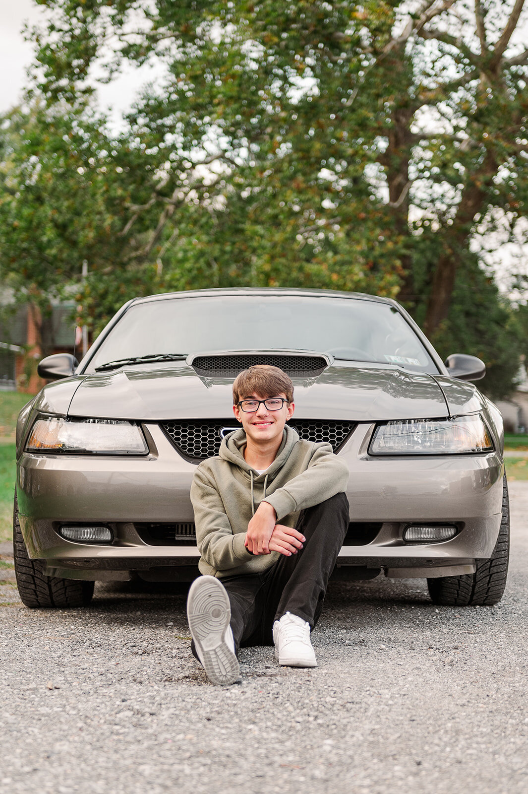 senior boy sitting on the ground in from of his mustang