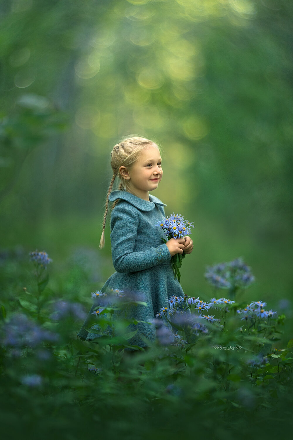 Girl in blue wool dress holding blue flowers, standing in a flower patch.