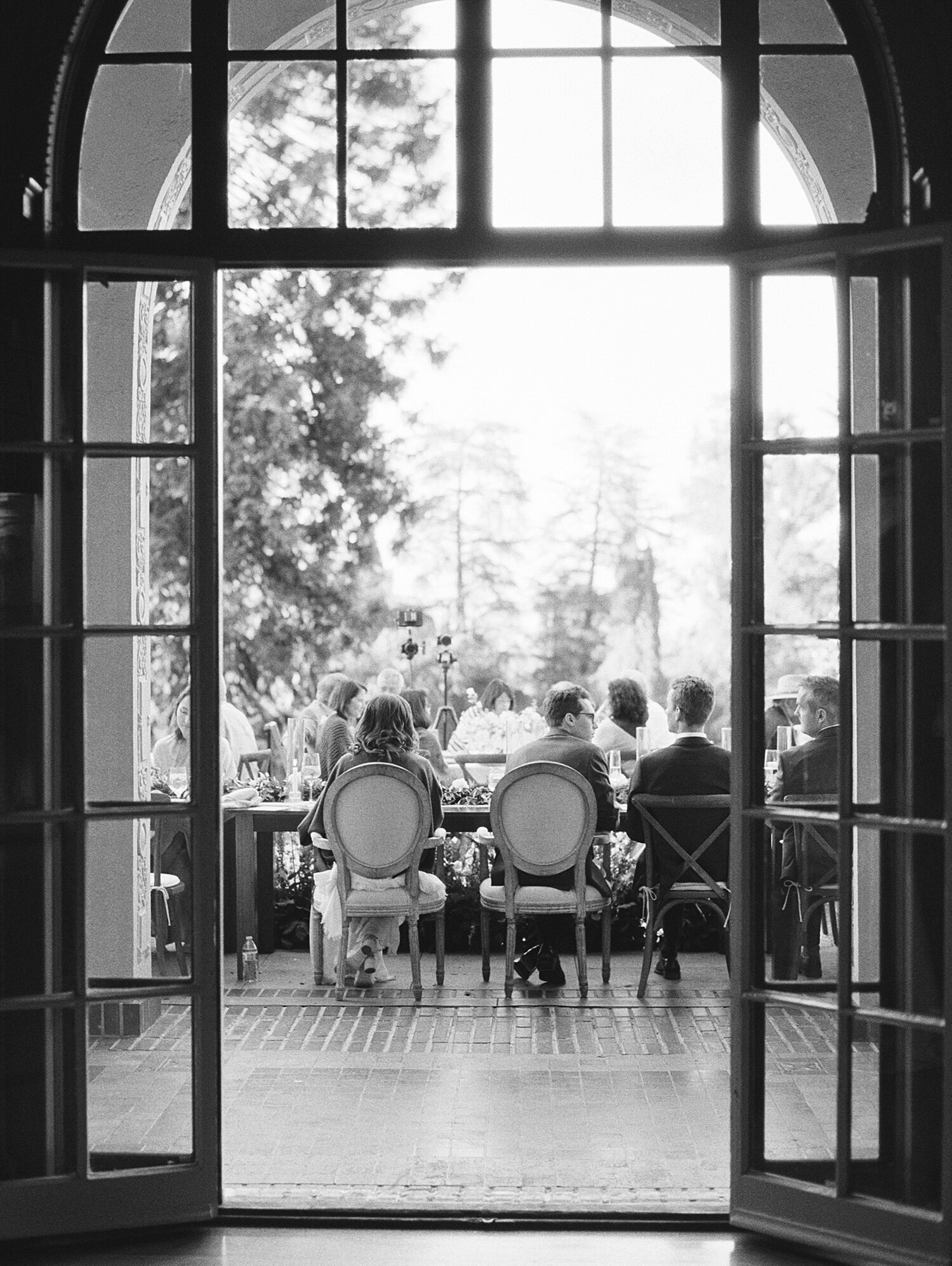 black and white candid film photo from behind bride and grooms table through large windows