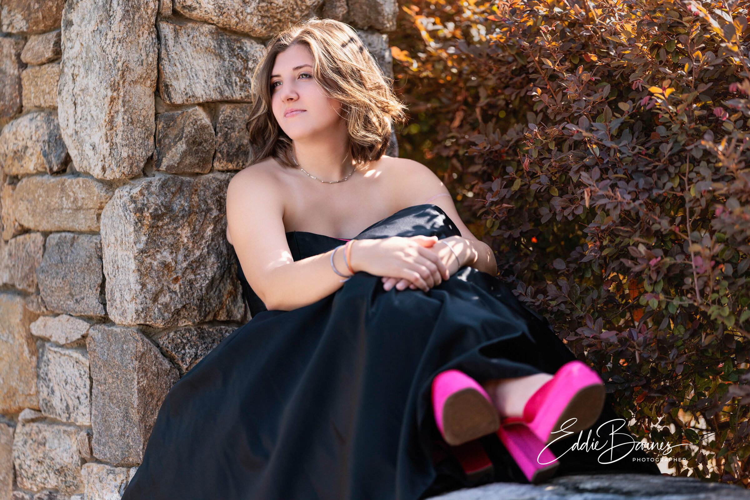 Young woman smiling confidently in a strapless black gown with pink heels during an outdoor senior photo session in Greenville, South Carolina, captured by Tytanium3 Photography.