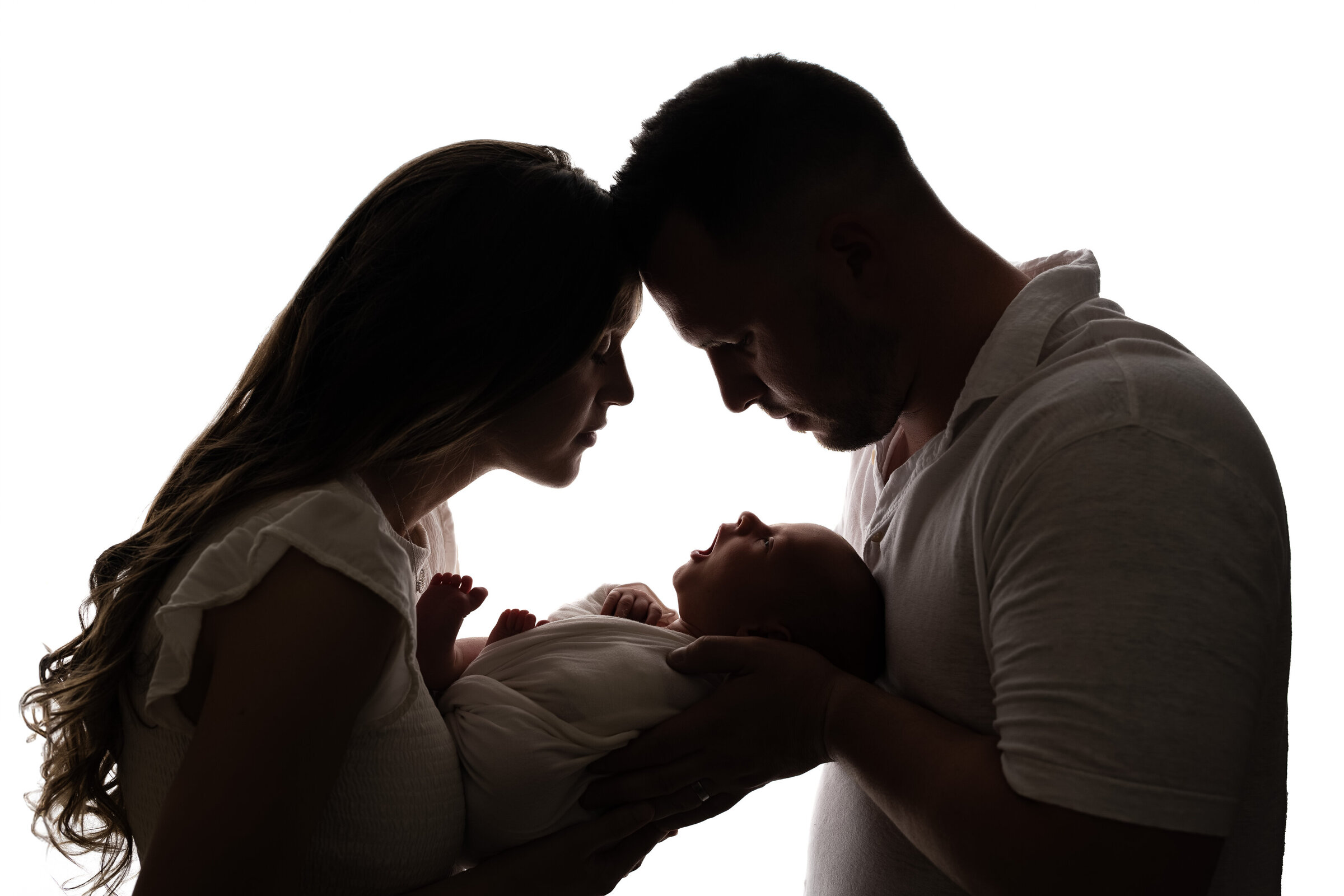 Backlit silhouette of parents holding their newborn baby between them, foreheads gently touching in a moment of connection.