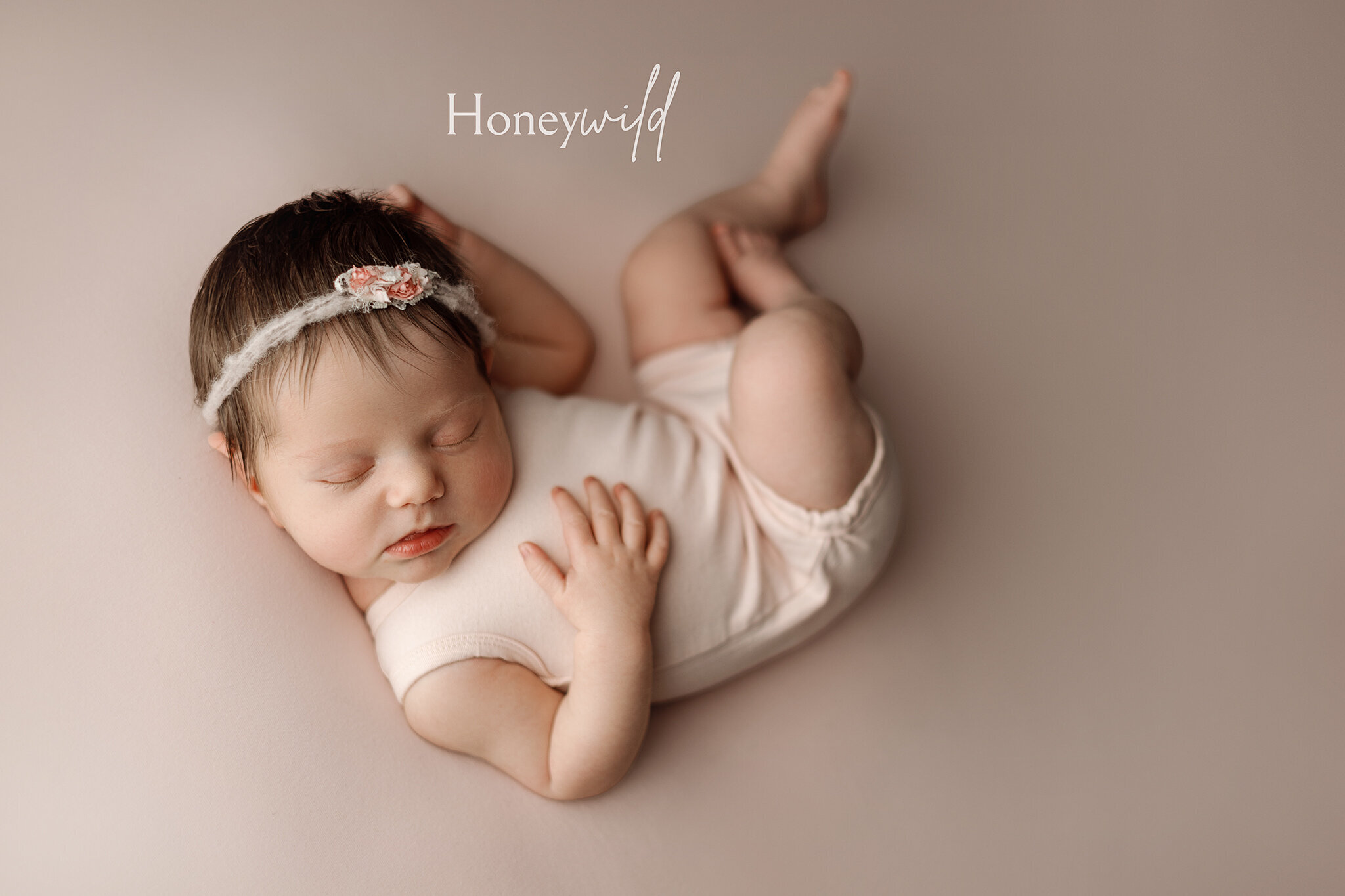 Grand Rapids newborn photography by Honeywild Photo: Newborn baby peacefully sleeping on a soft white blanket, wearing a rainbow knit hat. Capturing warm, timeless moments with professional newborn photography in Grand Rapids, MI.