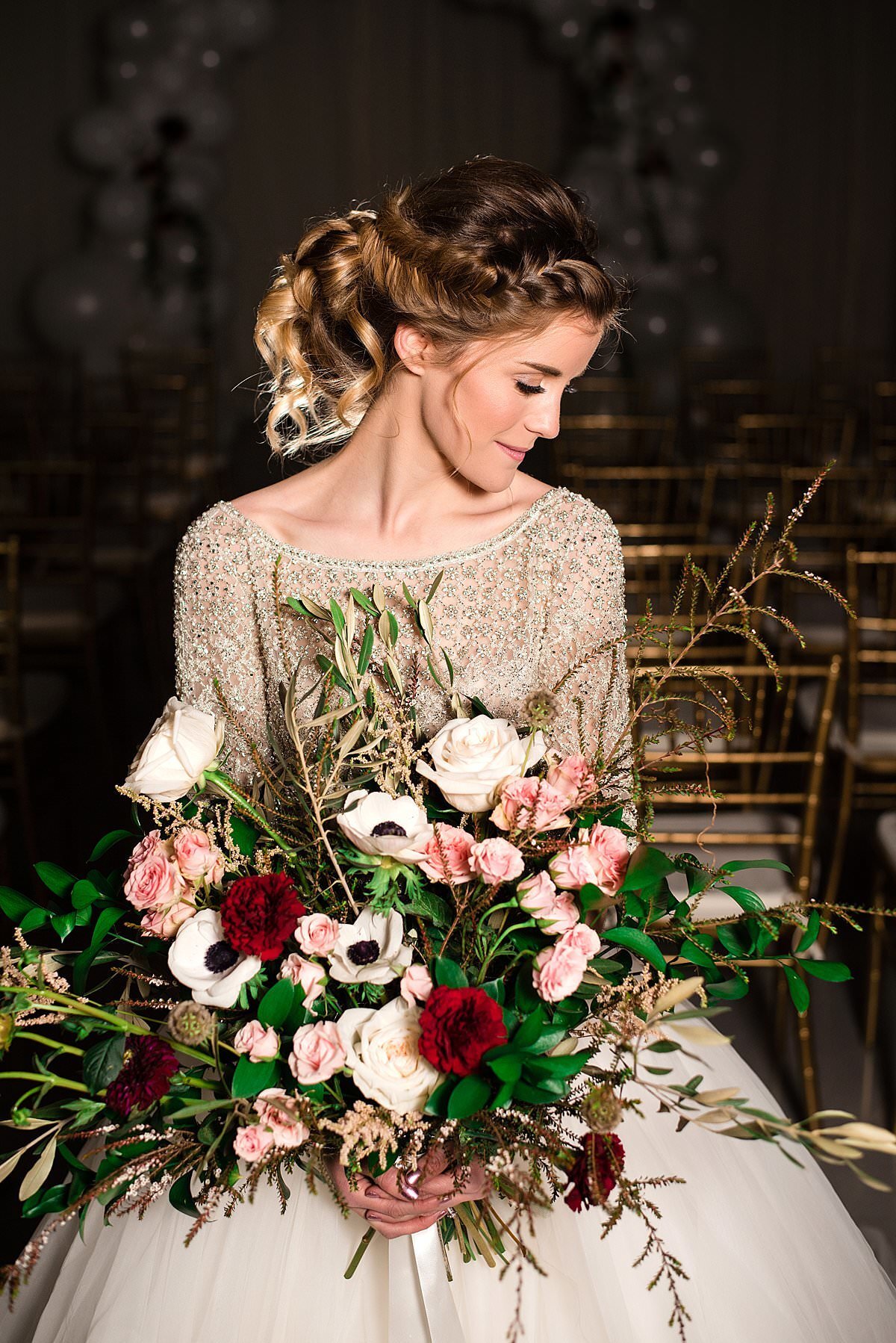 Bride with an intricately braided updo holding a large bouquet filled with anemones, pink and burgundy flowers