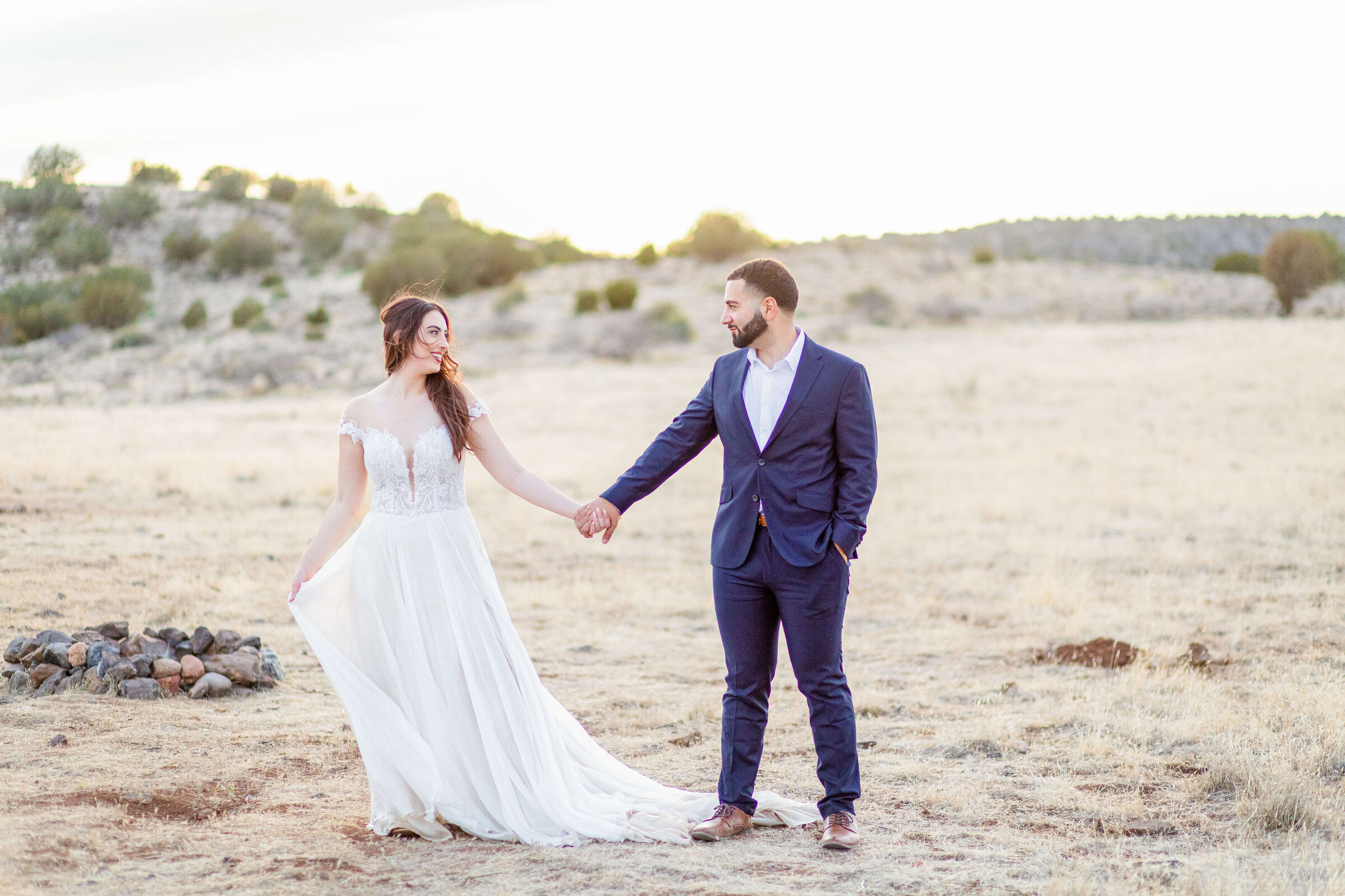A bride and groom hold hands in the middle of the desert in Arizona. The sun is setting and the field is golden. Taken by a Cincinnati wedding photographer