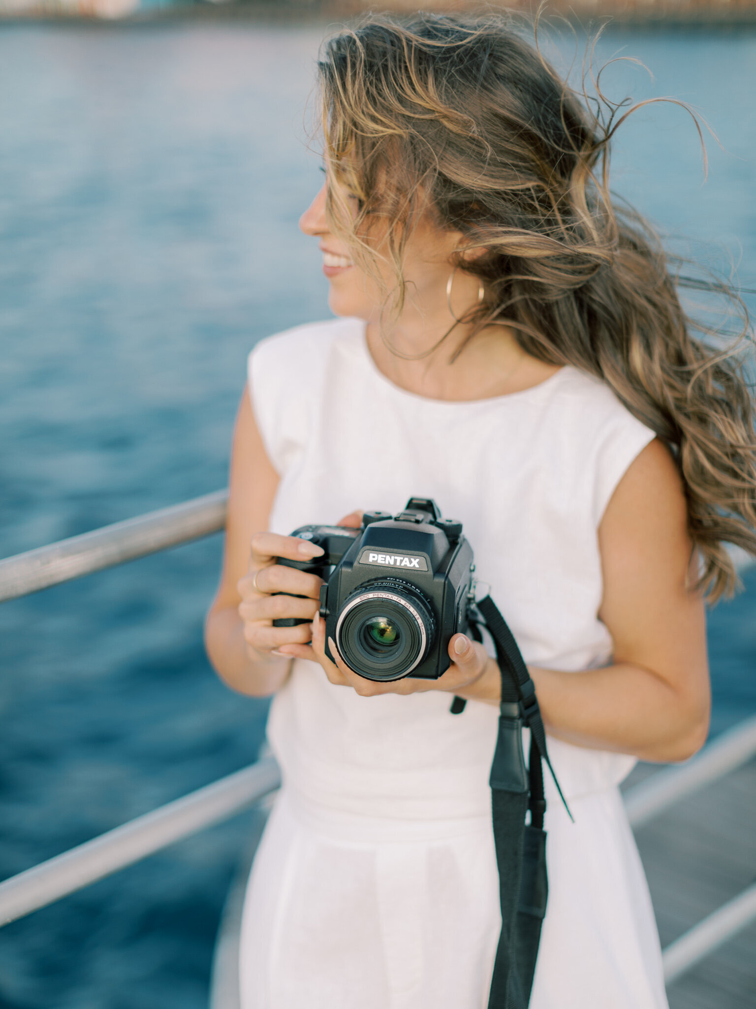 Brunette photographer Bailey Feeler dressed in white stands on bridge holding film camera