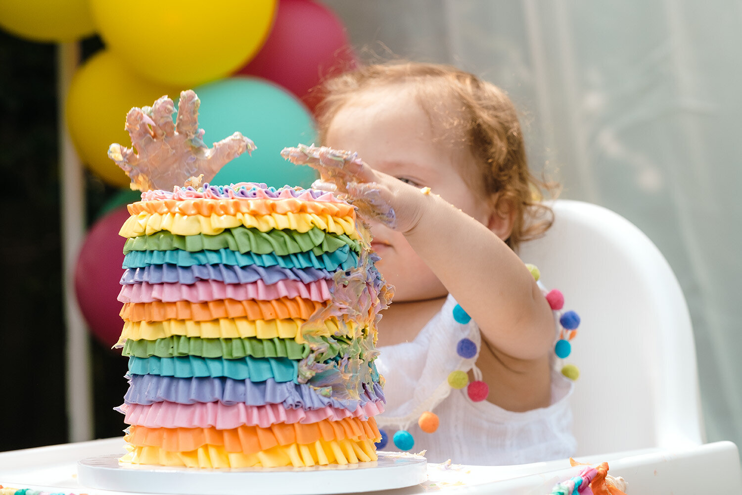 Bay Area first birthday party photographer captures a baby girl with her hands in the smash cake during her birthday celebration