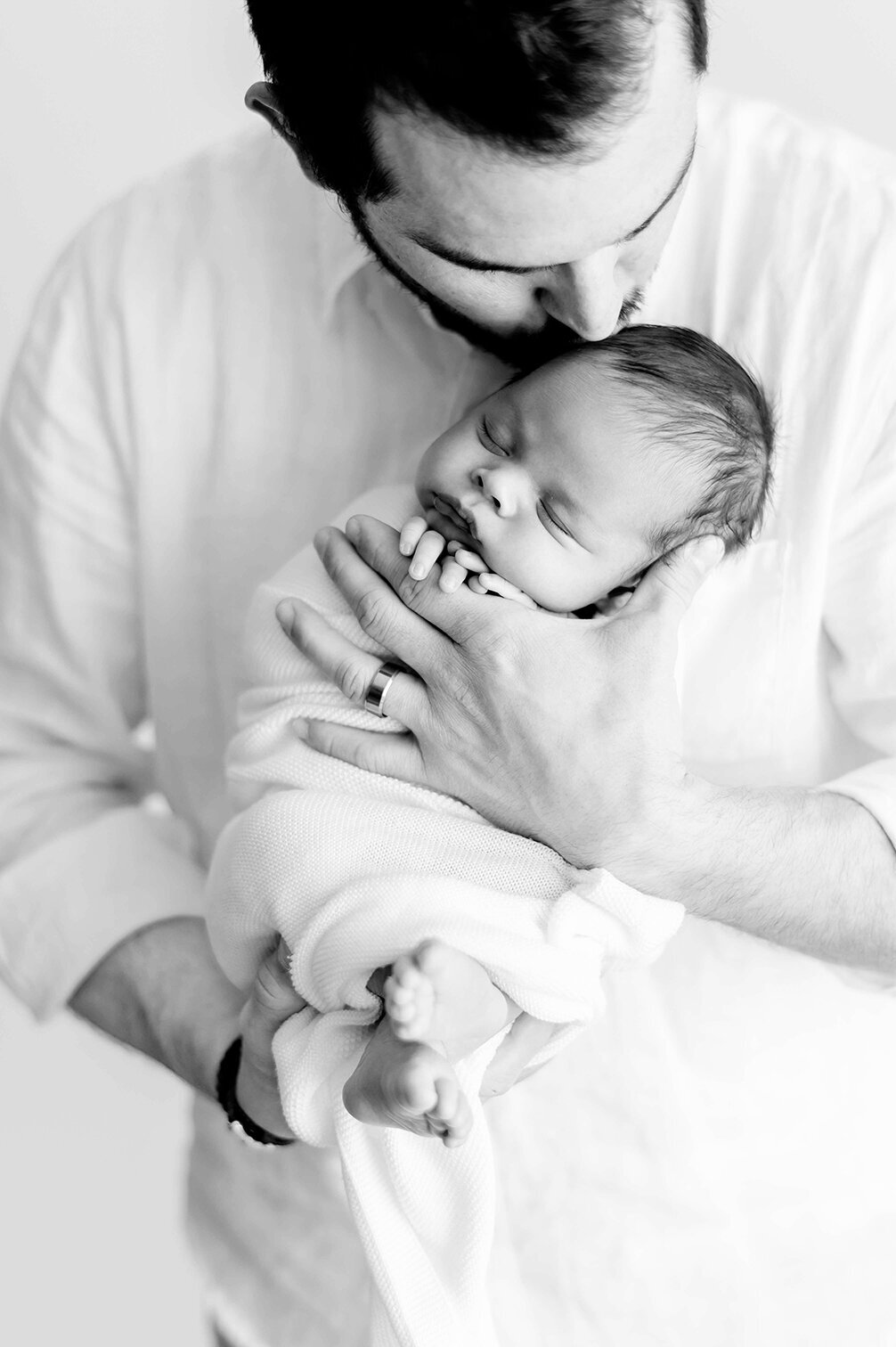 black and white image of a father kissing his newborn baby  in Kristie Lloyd's Nashville newborn photography studio