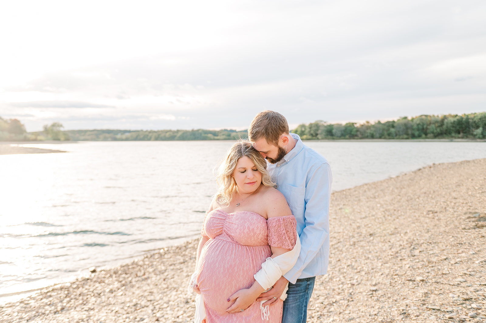 couple embracing by a lake during maternity session with sunset in baltimore md