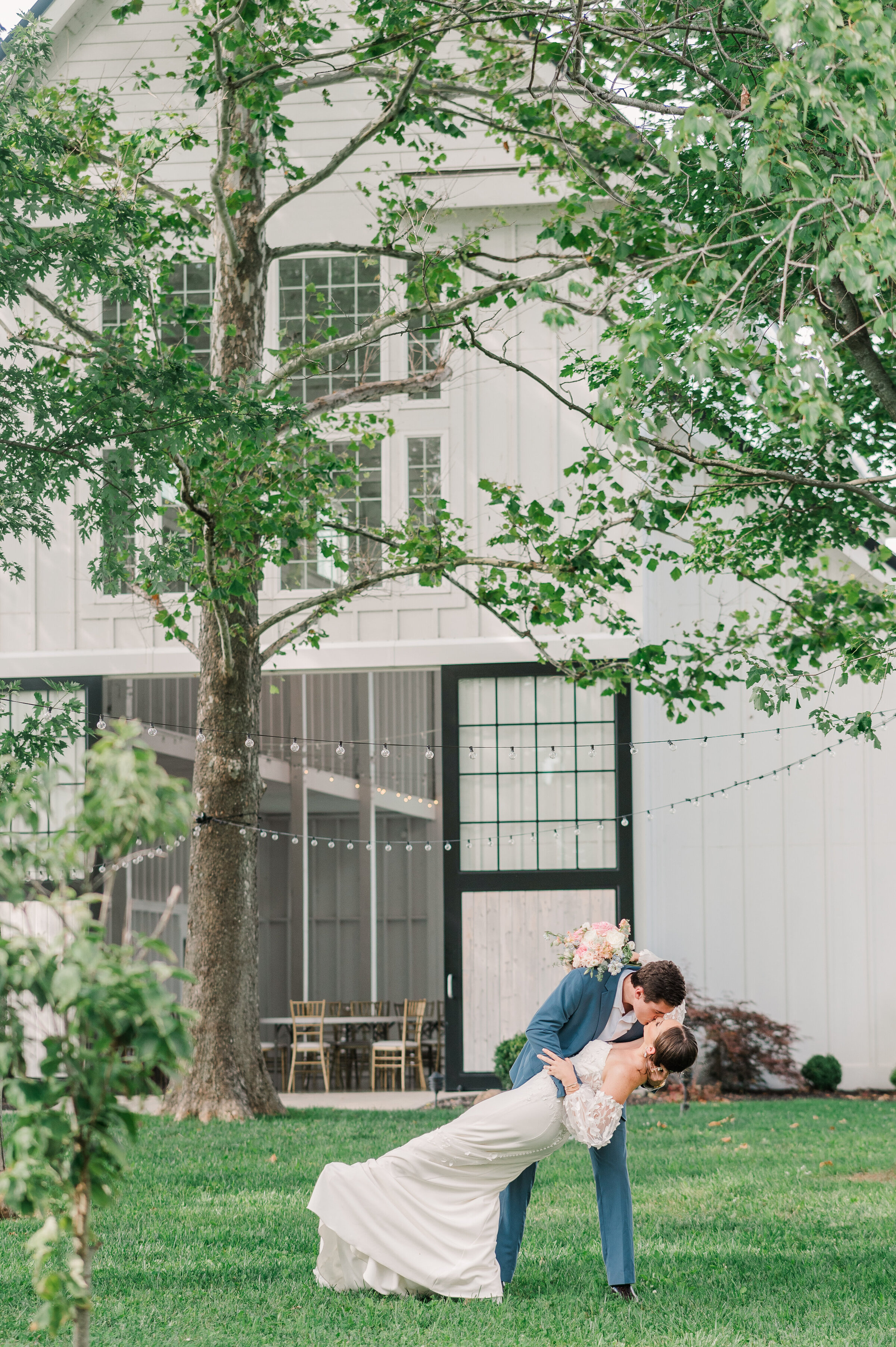 Groom dips bride for a kiss in front of Ashford Acres Inn Event barn