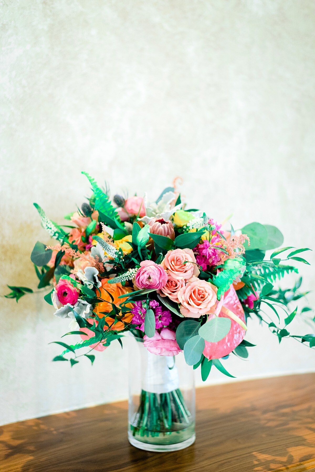 Vibrant colorful bride bouquet of pinks, oranges and eucalyptus sitting in a vase
