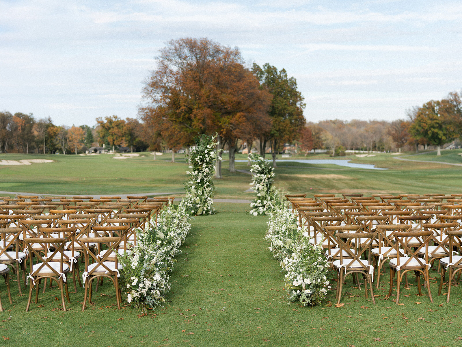 Outdoor country wedding with asymmetrical broken arch and river of green & white flowers lining aisle.  
