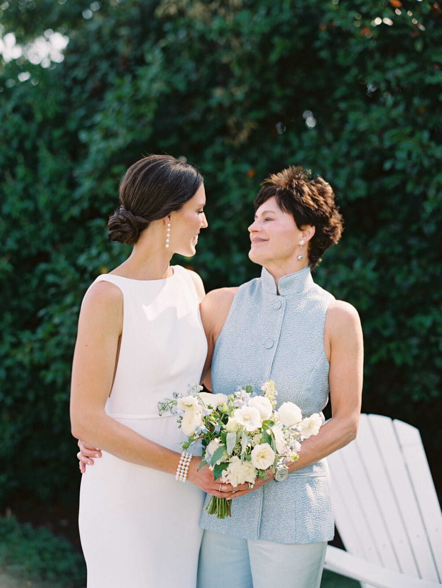 bride and her mom embracing and looking at one another with greenery background