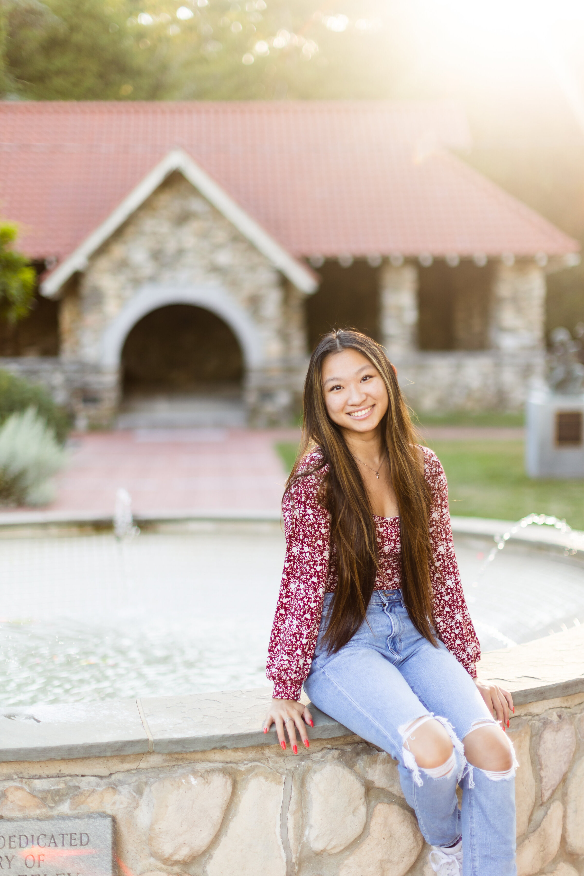 Summer senior girl sits on fountain and smiles during senior session at Greeley Park in Nashua, New Hampshire