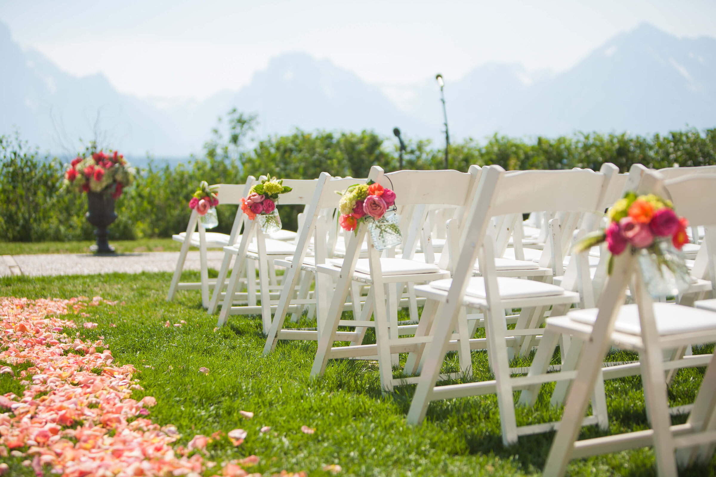 Outdoor Ceremony at Jackson Lake Lodge White chairs line a grassy aisle covered in rose petals, leading to a floral-adorned altar. The Grand Tetons provide a breathtaking backdrop for this Jackson Lake Lodge wedding ceremony.