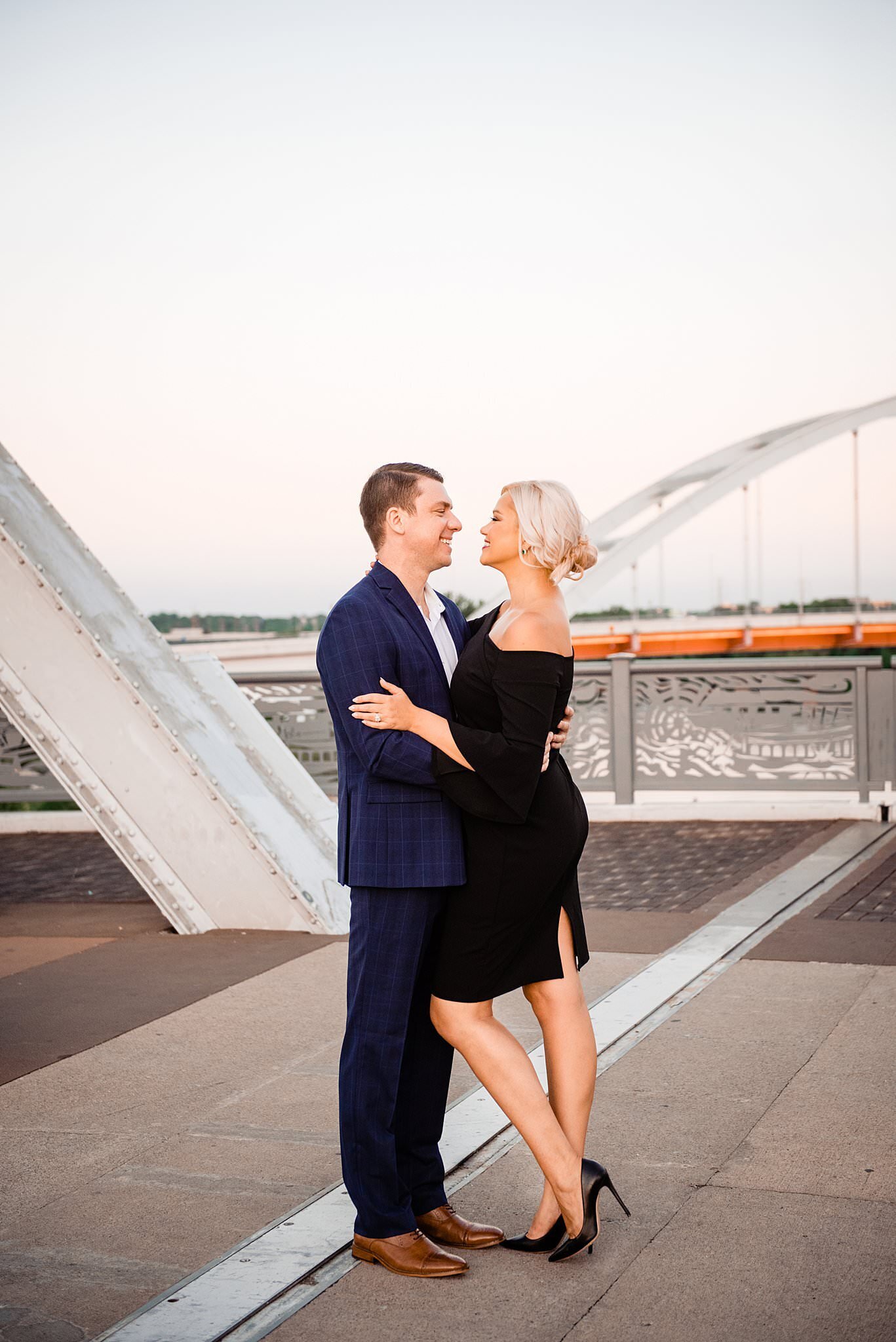 Couple wearing a suit and black dress standing on john schneider bridge
