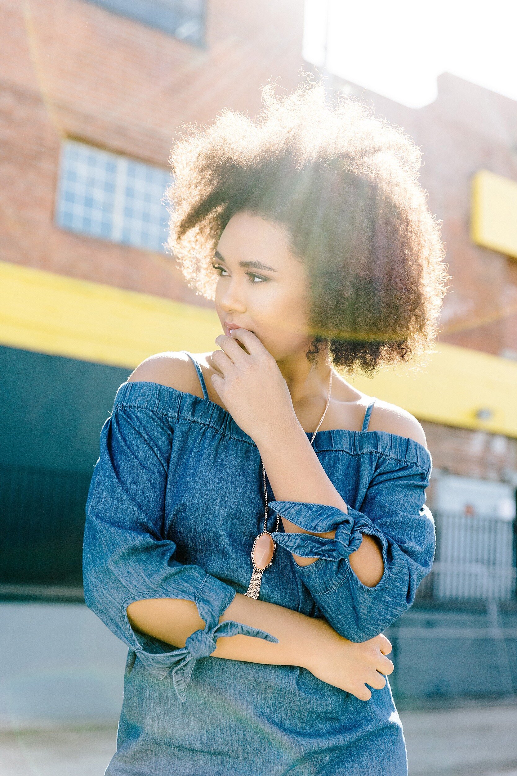 High school senior portrait in Los Angeles, girl in denim off-the-shoulder dress with natural curly hair, editorial urban photography