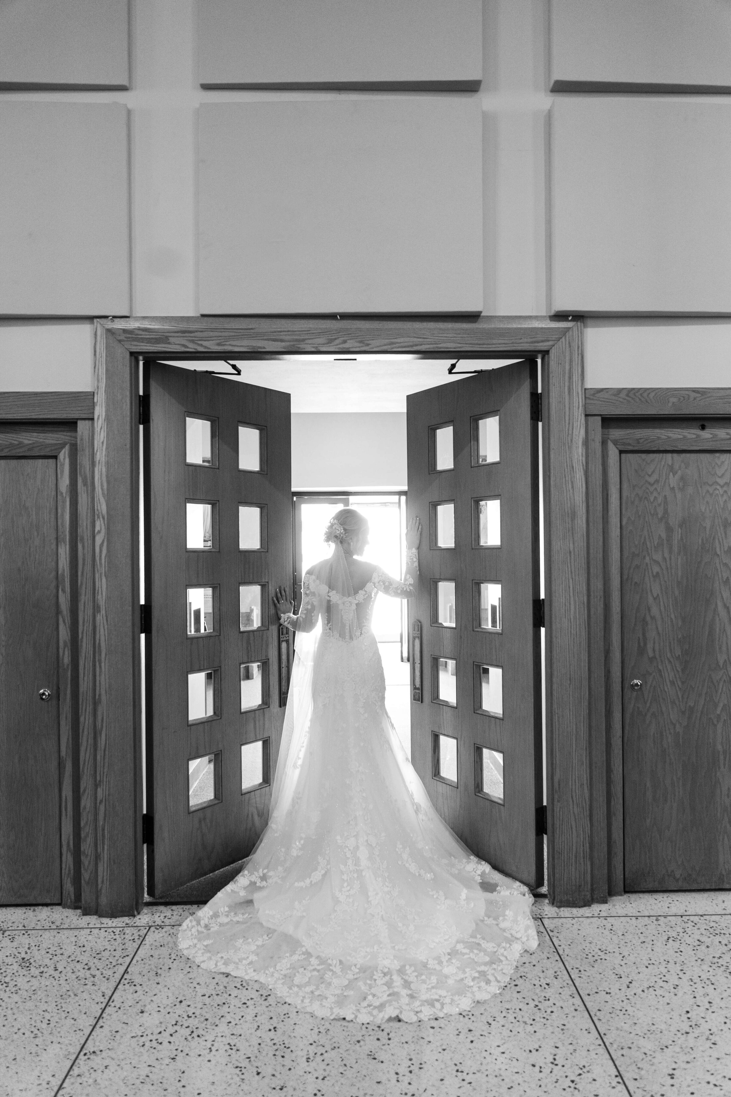 A bride stands in the doorway of her church. It is a black and white photo.