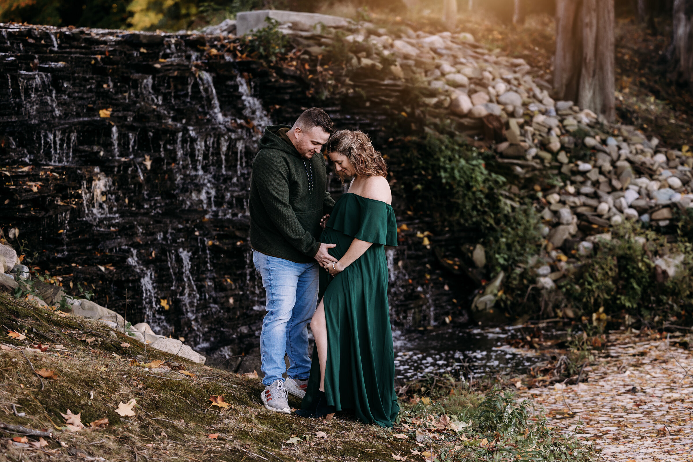 Expecting couple cradle their baby in front of a waterfall