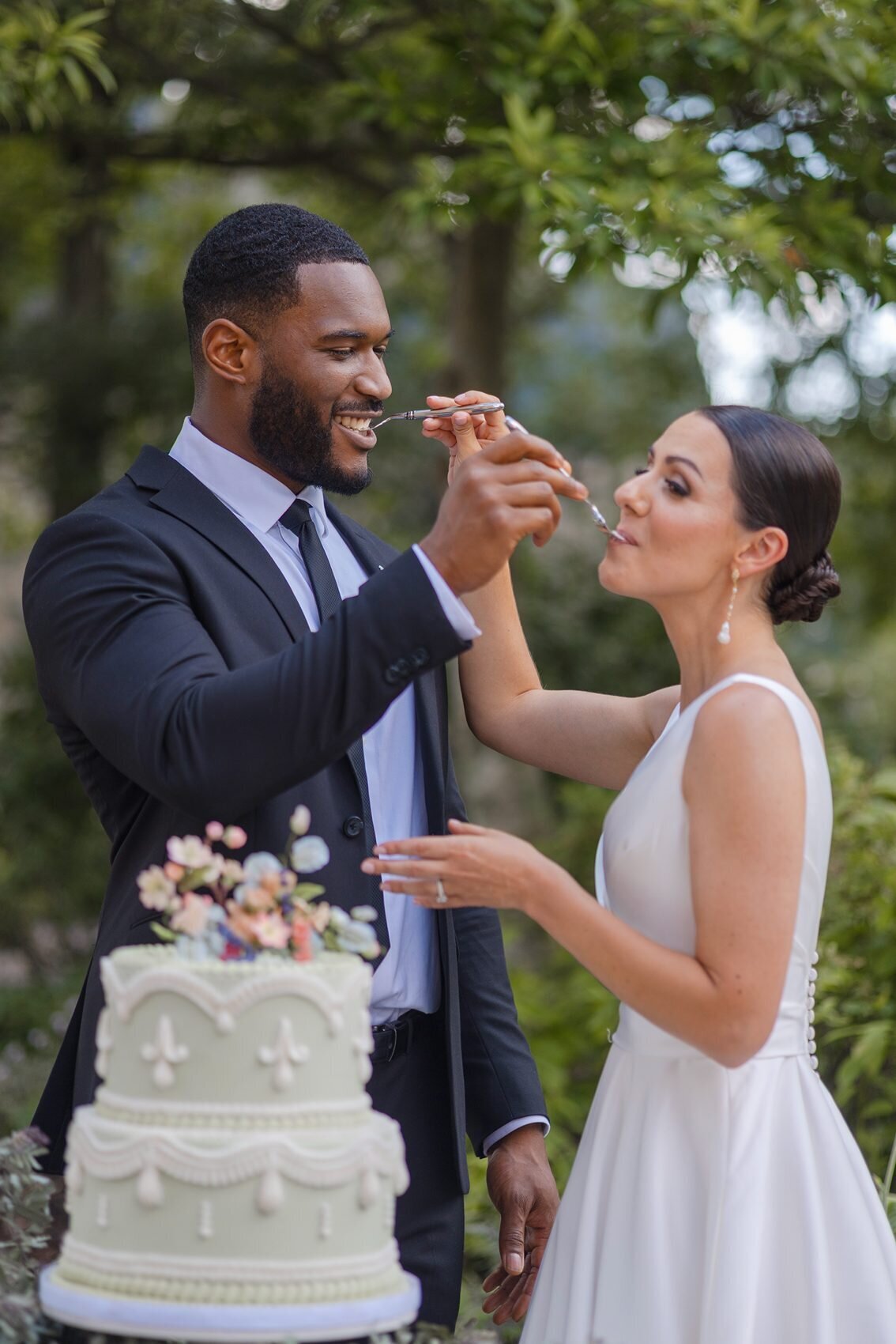 Elegant inter-racial couple photograph of black groom feeding his caucasian bride cake with the spoon.