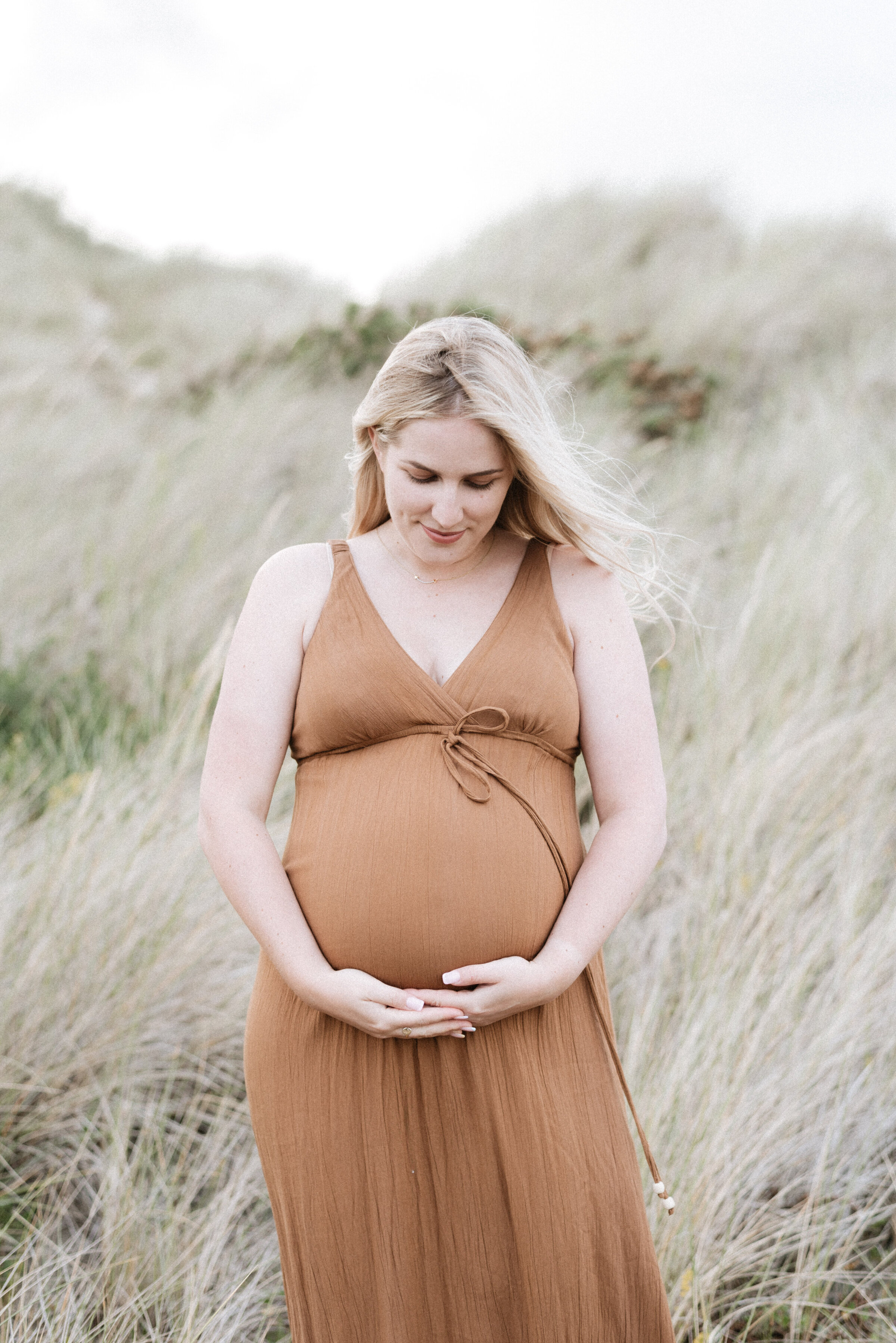 A mother looking down and pregnant stomach at the beach at a maternity photoshoot in Billingshurst