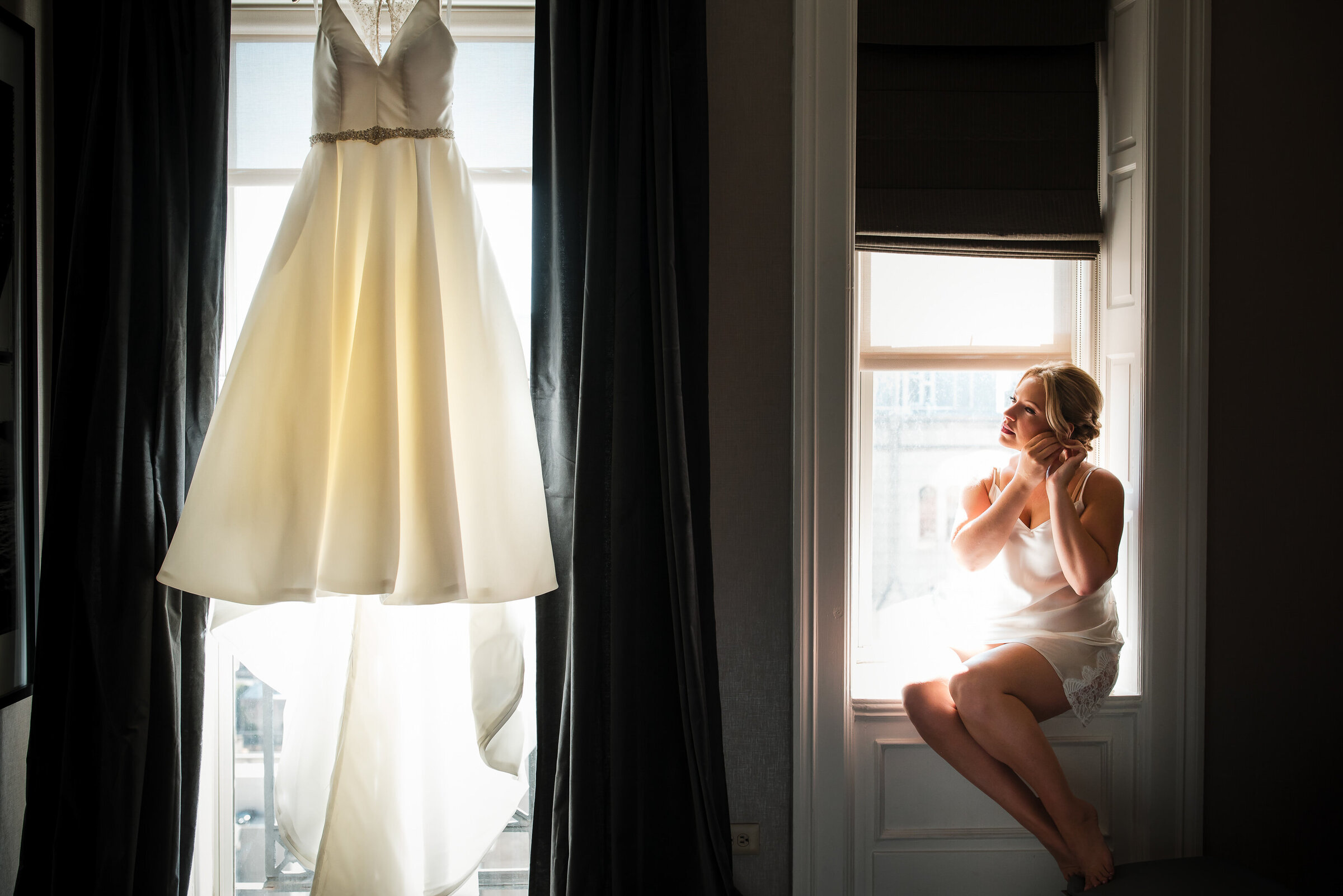 Bride sitting by the window looking at her wedding dress at Bellevue Hotel in Philadelphia