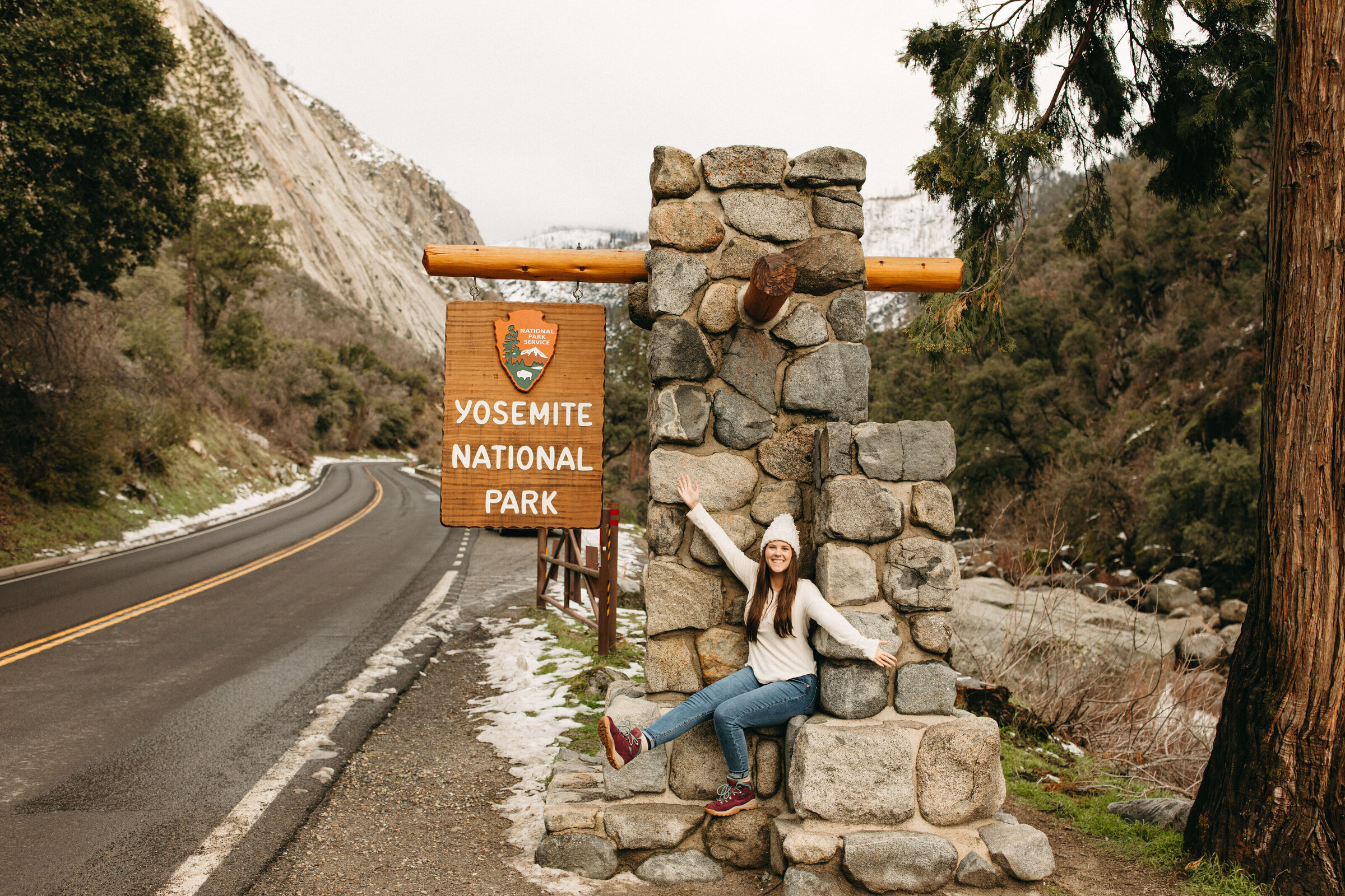 A girl sitting in front of the welcome sign in Yosemite National Park.