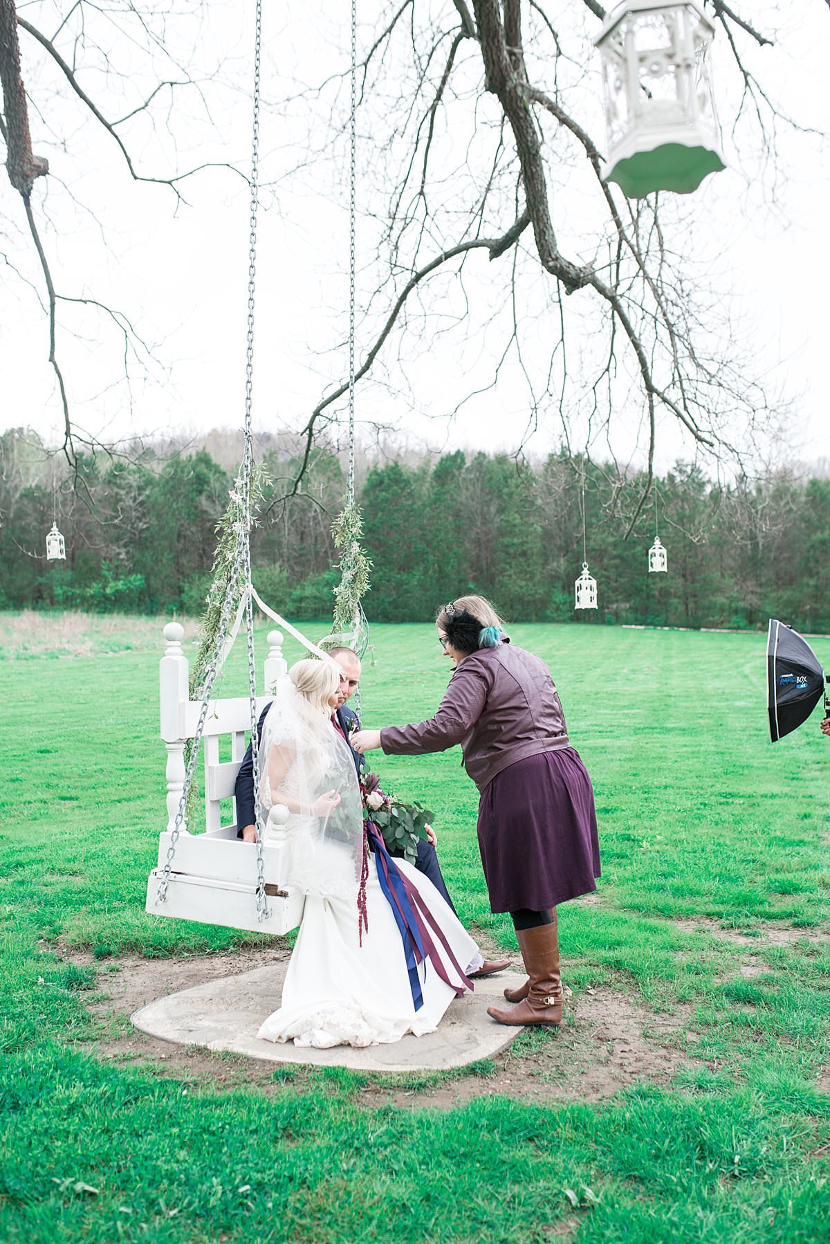 Behind the scenes photo of wedding photographer adjusting brides veil during couples portraits on the swing at Drakewood Farms
