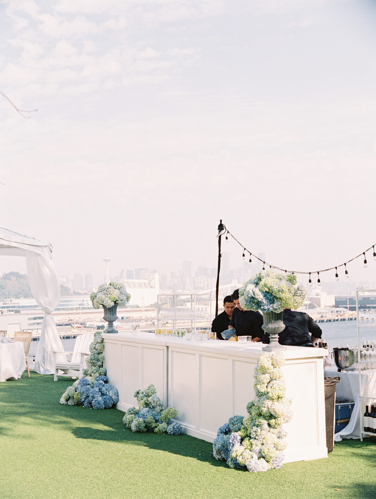 white bar rental for wedding with lush large blue hydrangea's around it