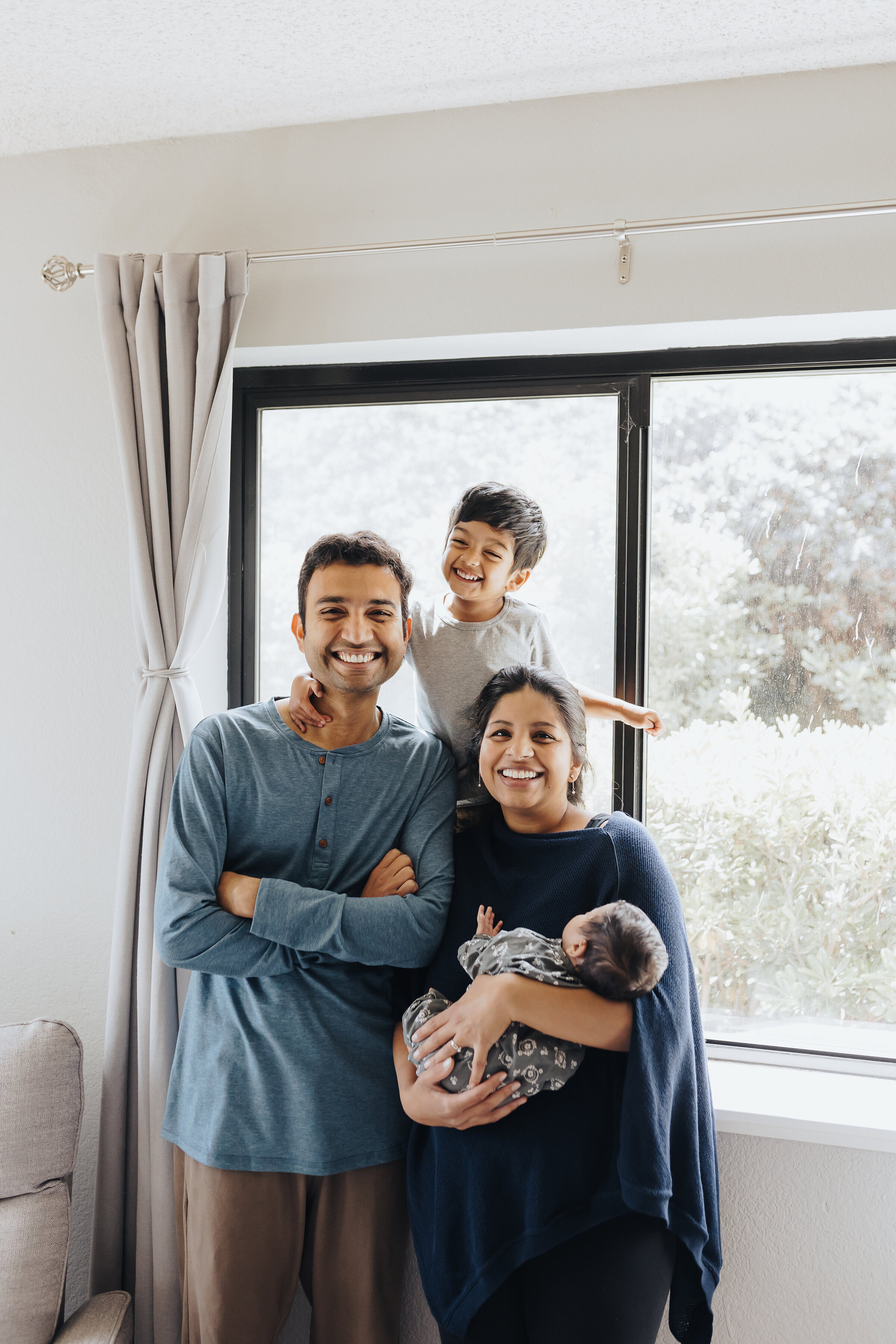 Family stands in the window of their bedroom during a newborn session at home