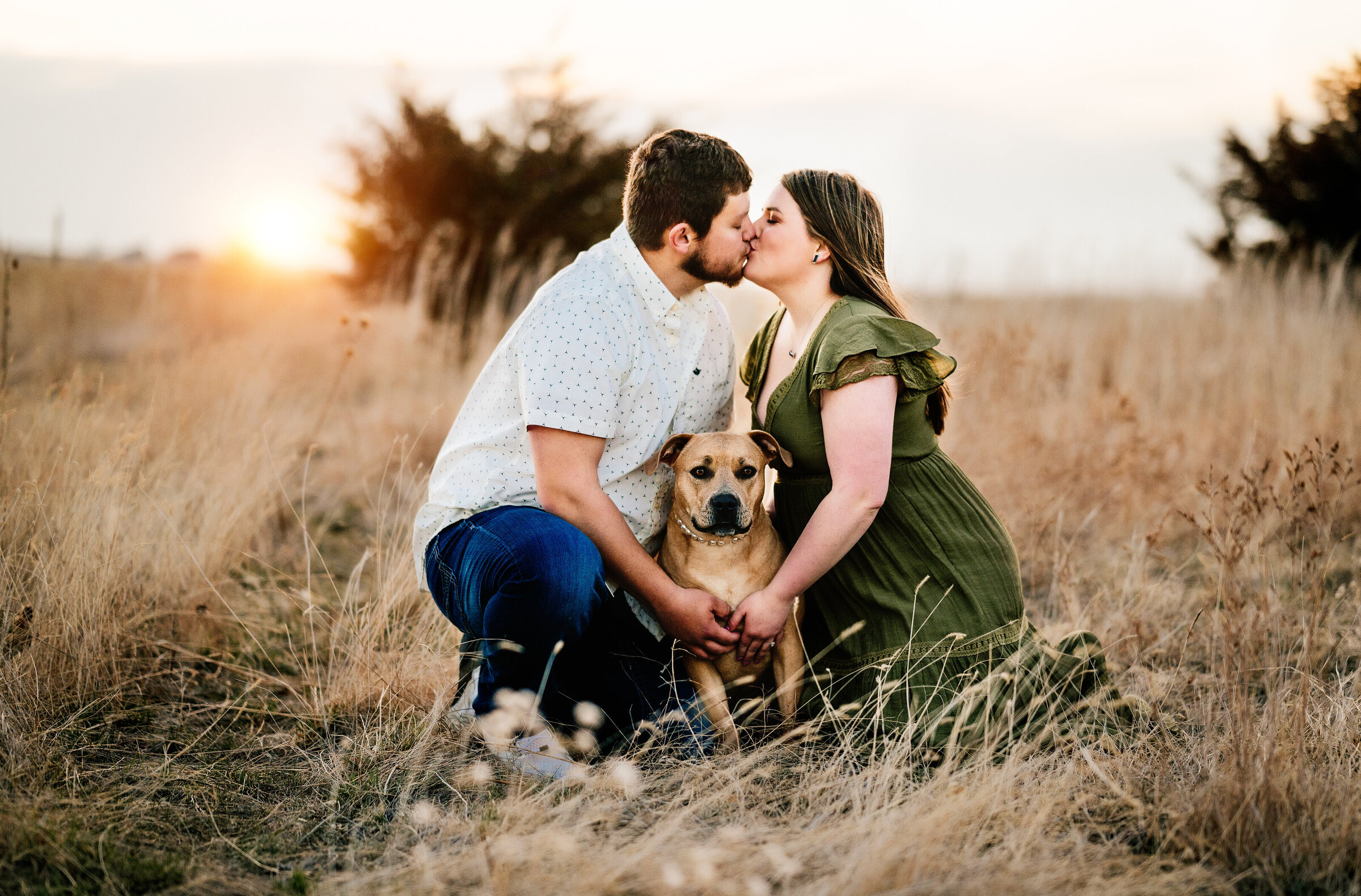 Couple kisses over their dog in field