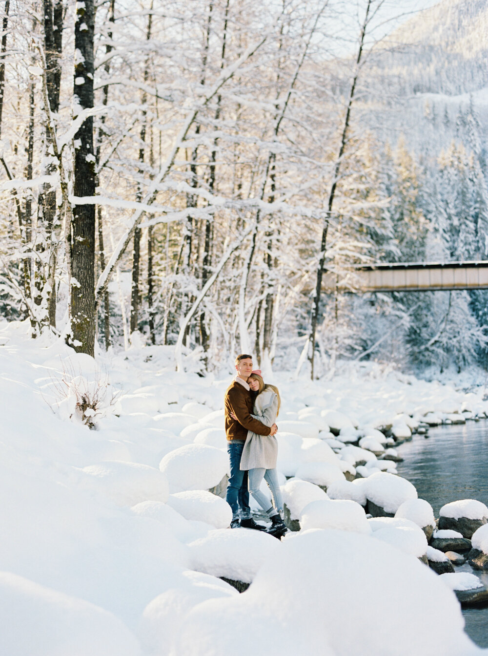 snow filled river rocks with goldne sun shining through as couple hugs