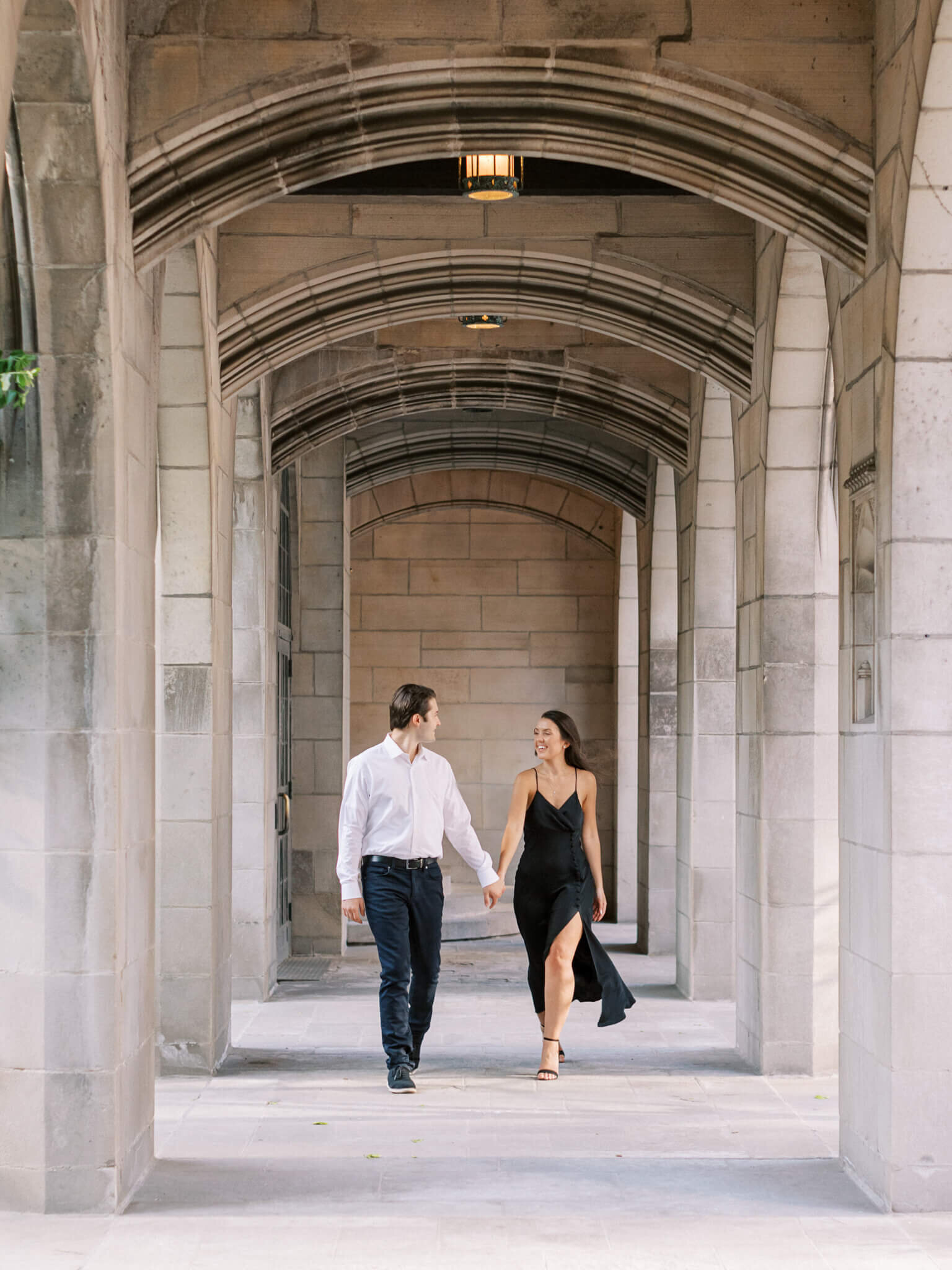 Engaged couple walking through stone walkway holding hands