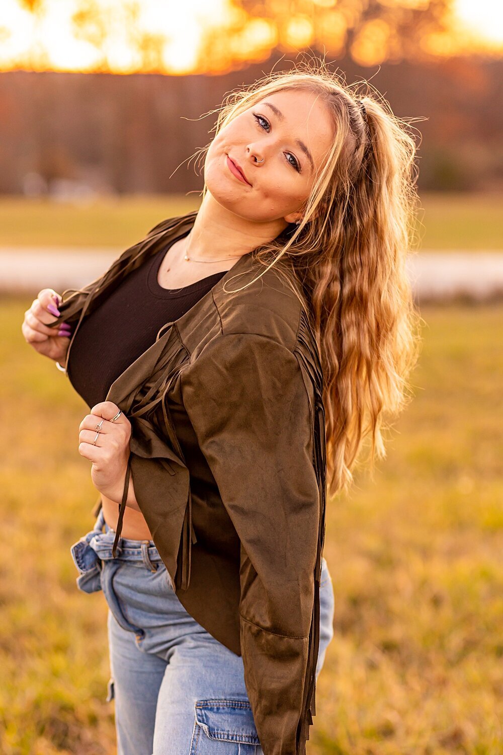 Fall senior girl holds green jacket and smiles during sunset senior session in Bedford, New Hampshire