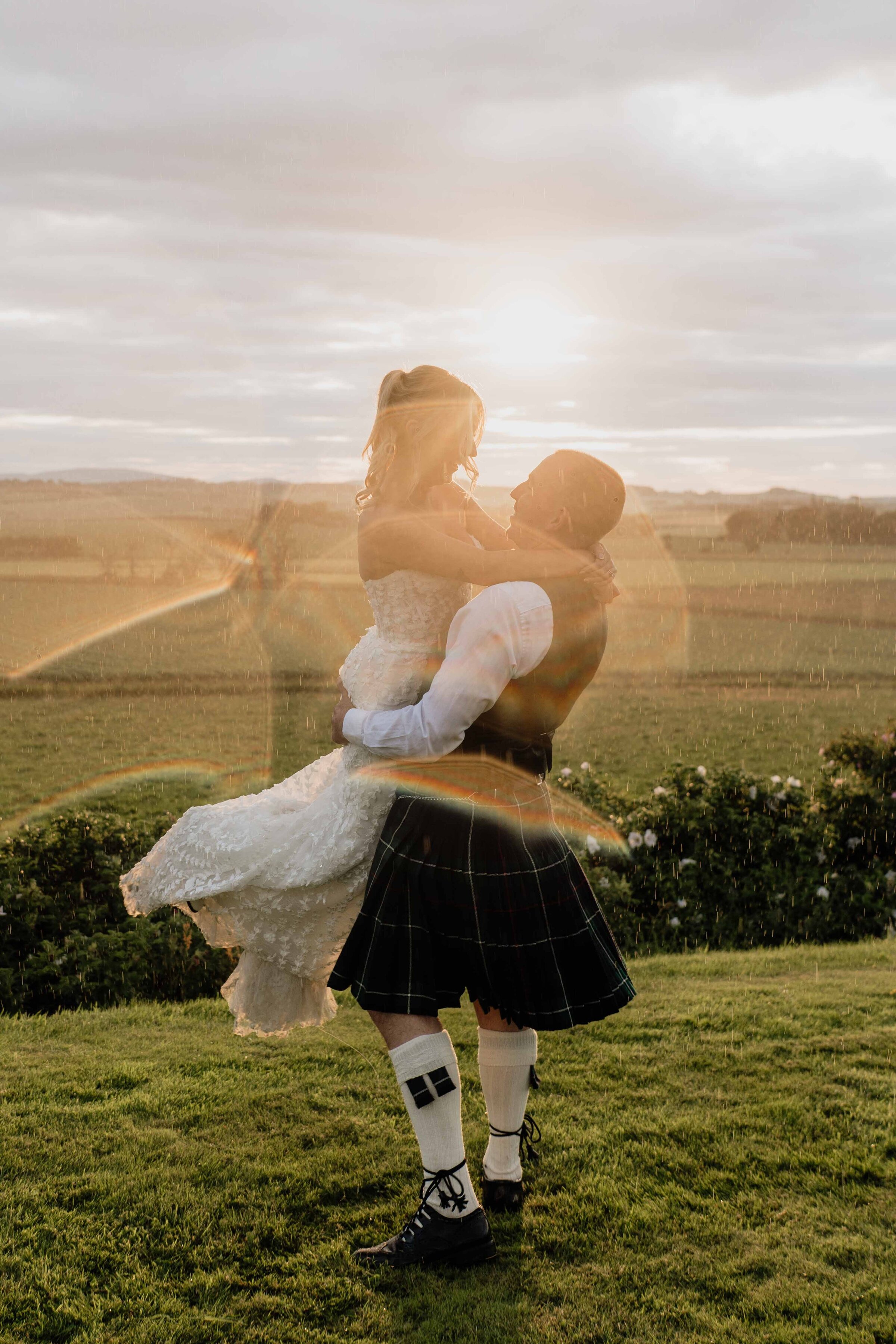 A bride and groom are photographed spinning each other at Barra Barn. The sun sets across the Aberdeenshire landscape behind them.