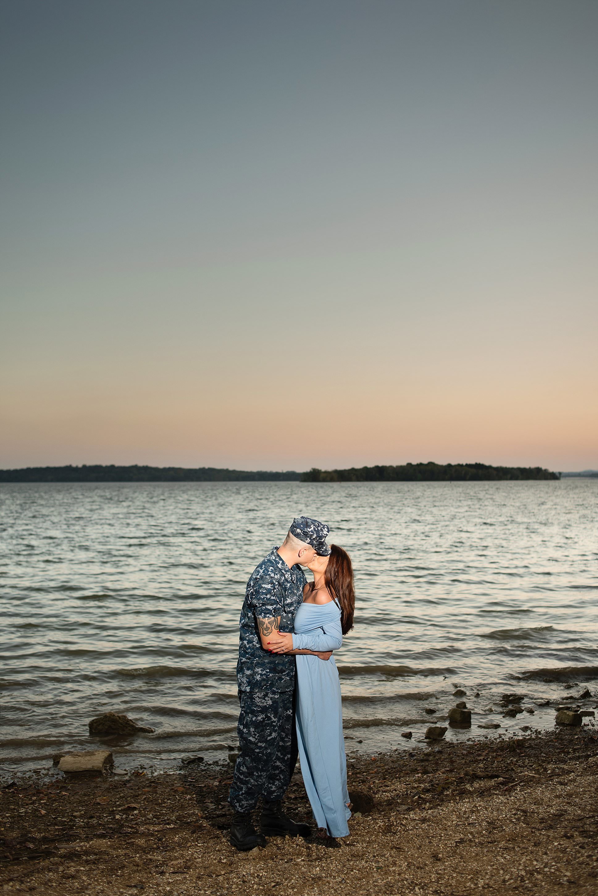 Engagement photo of groom in military  attire and his fiance in a baby blue ankle length dress standing on the lakefront during sunset at Long Hunter State Park