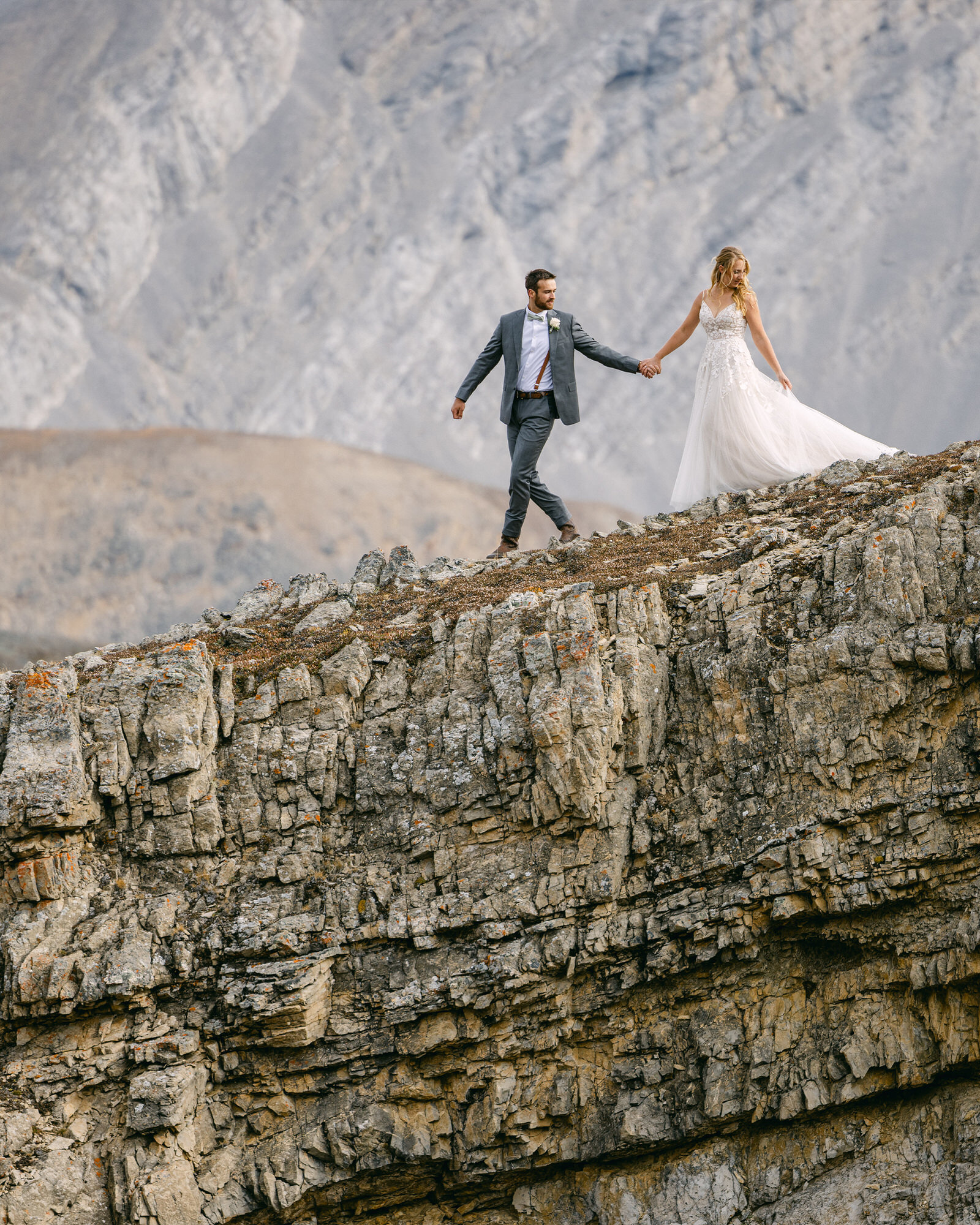 A truly epic photograph capturing the bride and groom as they walk down a rugged mountainside in Banff National Park, surrounded by towering peaks. Immersed in the breathtaking wilderness, they take in the surreal beauty of their surroundings, embracing the awe-inspiring moment of their unforgettable wedding adventure.