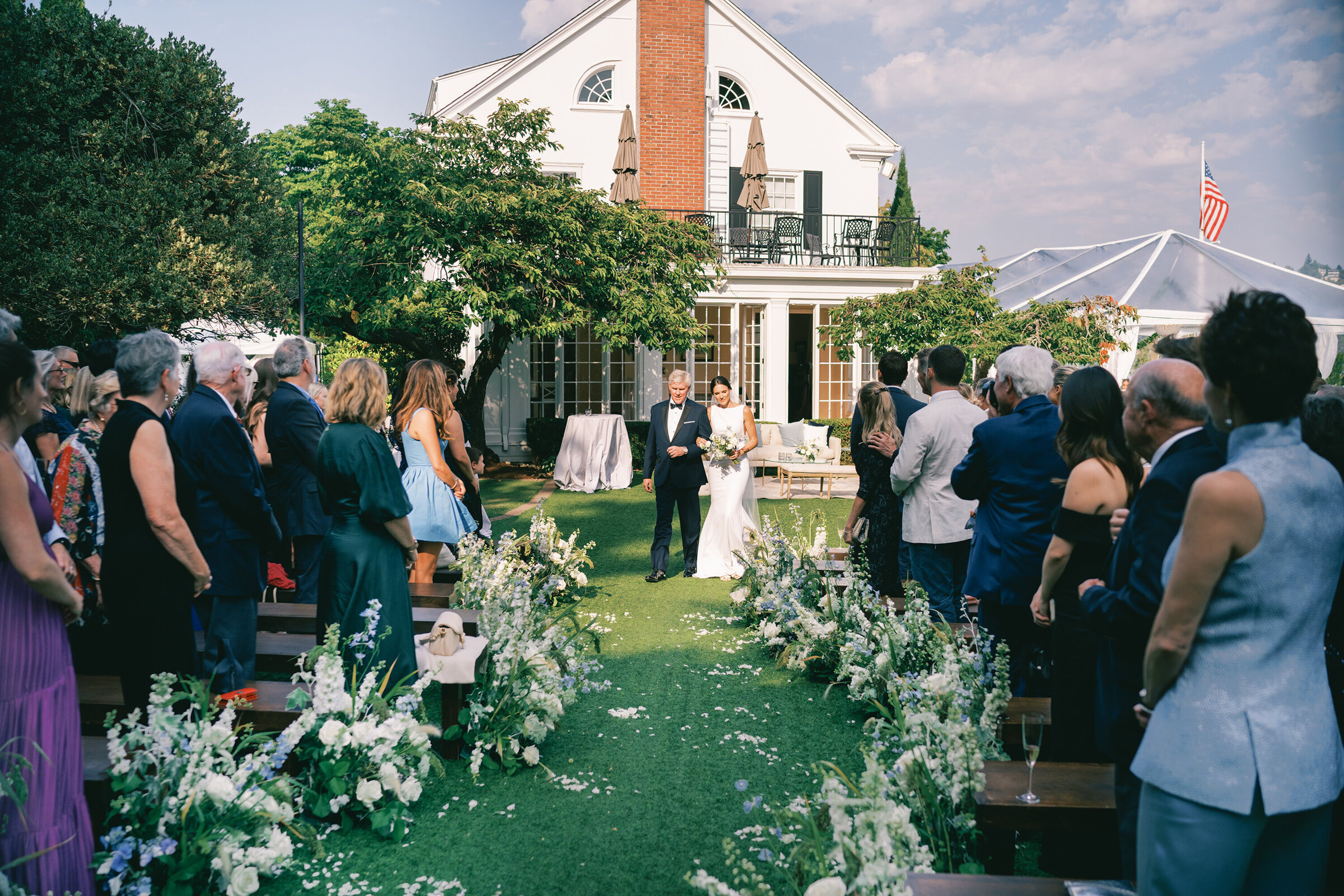 wide angel photo of bride walking down the aisle on green grass with historic venue behind her