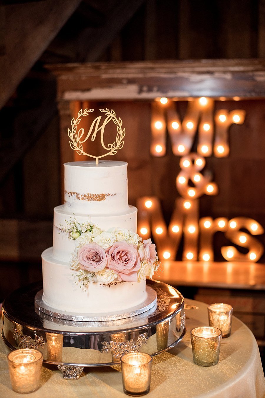 Three tier naked wedding cake with clush roses and Monogram cake topper, light up Mr and Mrs sign behind