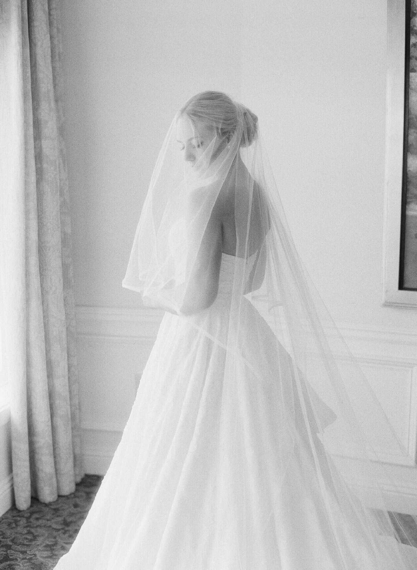 black and white film photo of bride with veil over her head in bridal suite