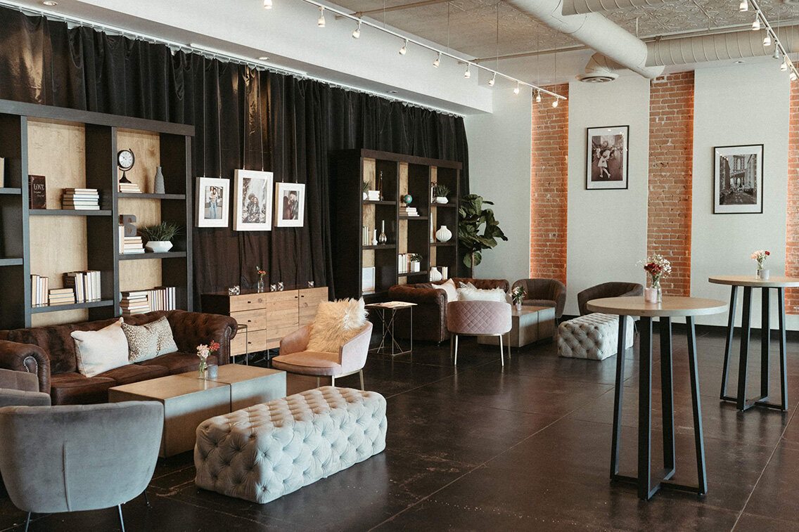 An inviting lounge space at SoHo63, a Chandler wedding and event venue, showcases a mix of tufted benches, velvet chairs, modern shelving, and exposed brick walls. The space is ideal for cocktail hours, wedding prep, or private events with a contemporary, boutique vibe.