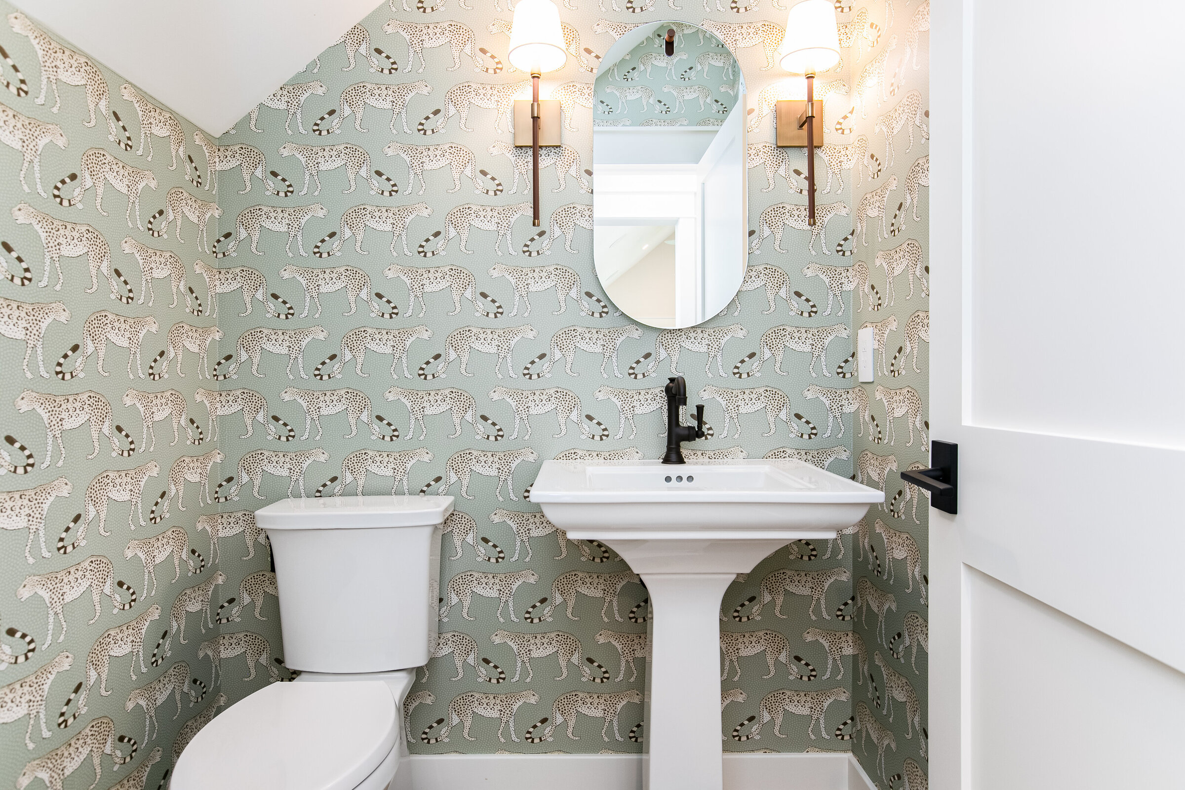 A chic and simple sink setup featuring a dainty mirror, stylish pendant lights, and bold wallpaper. The design combines subtle elegance with striking patterns, creating a beautifully balanced bathroom space.